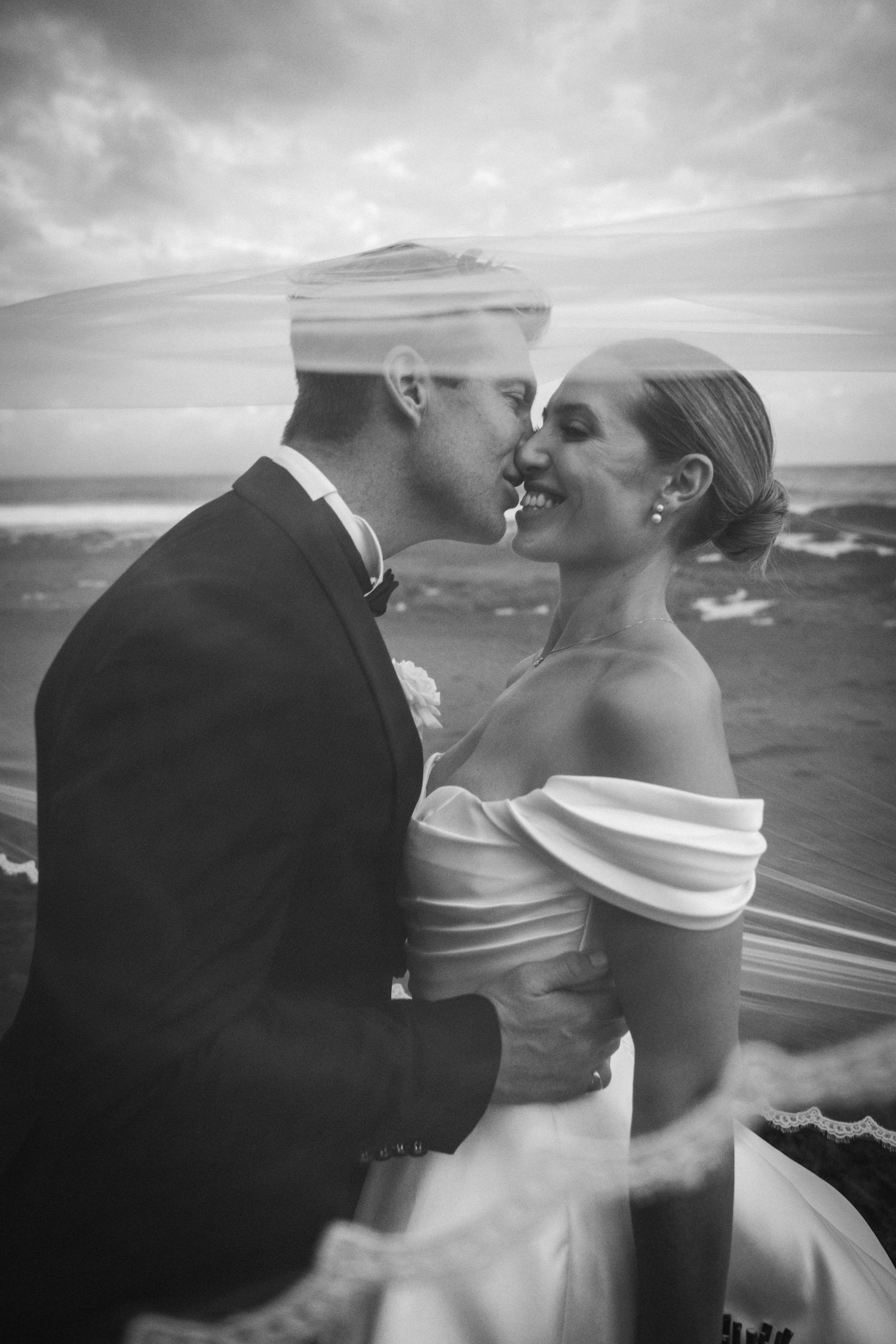 A romantic black and white wedding photo sequence showing a couple kissing on a beach with dramatic cloudy skies.