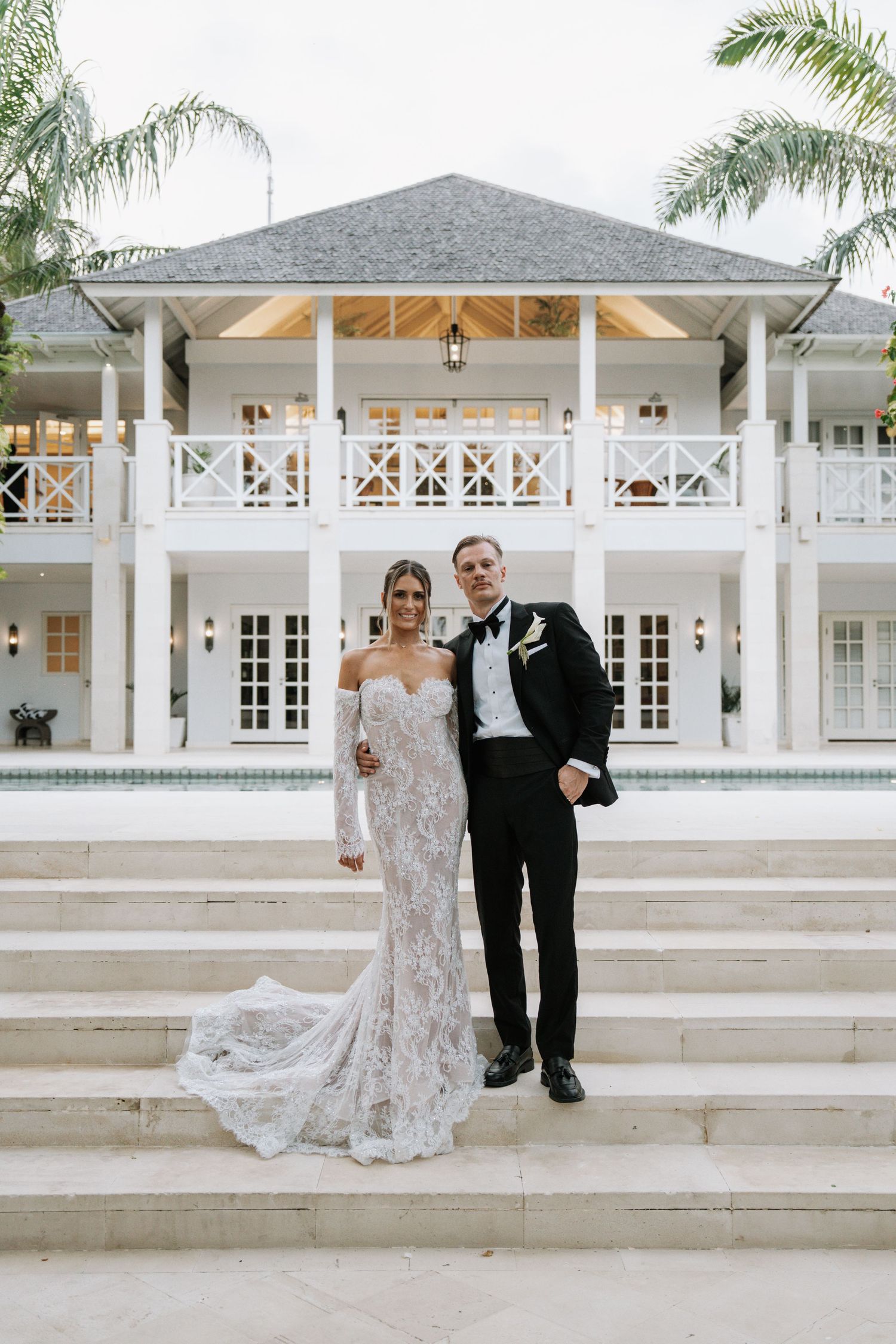 Elegant couple poses on white steps outside a classic colonial-style venue with white columns and French doors.
