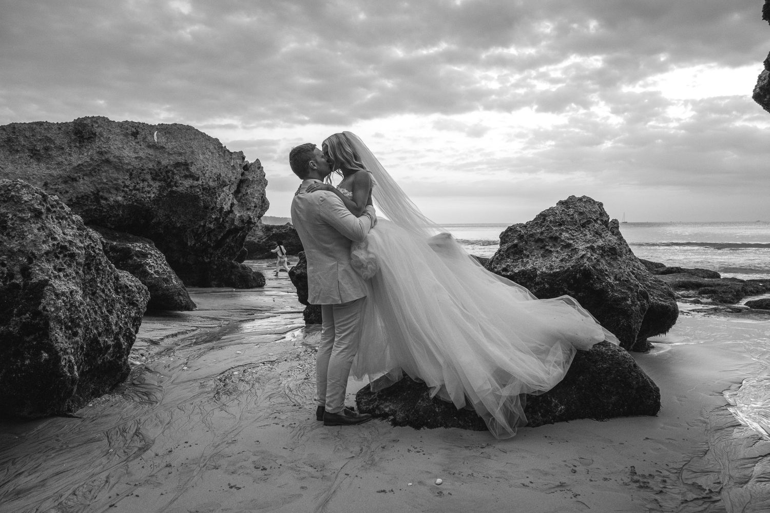 A dramatic black and white beach wedding photoshoot featuring rocky coastal landscapes and ocean waves.