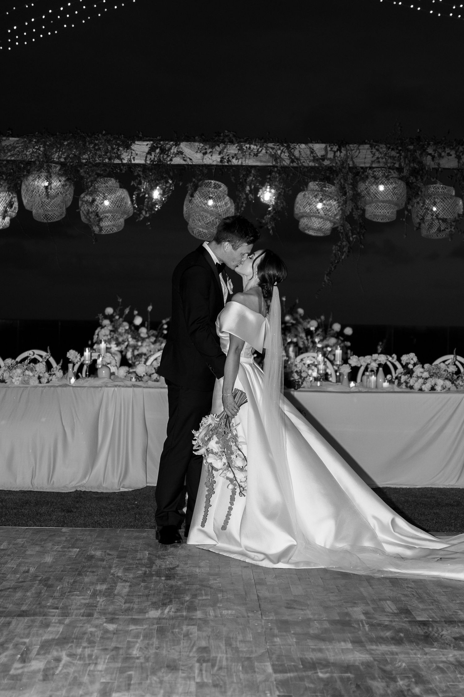 A couple shares a romantic moment on the dance floor at their wedding reception under decorative lanterns and twinkle lights.