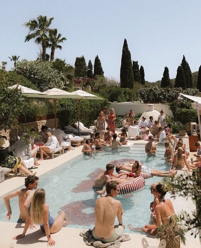 People enjoying a summer pool party with palm trees and cypress trees in a Mediterranean-style setting.