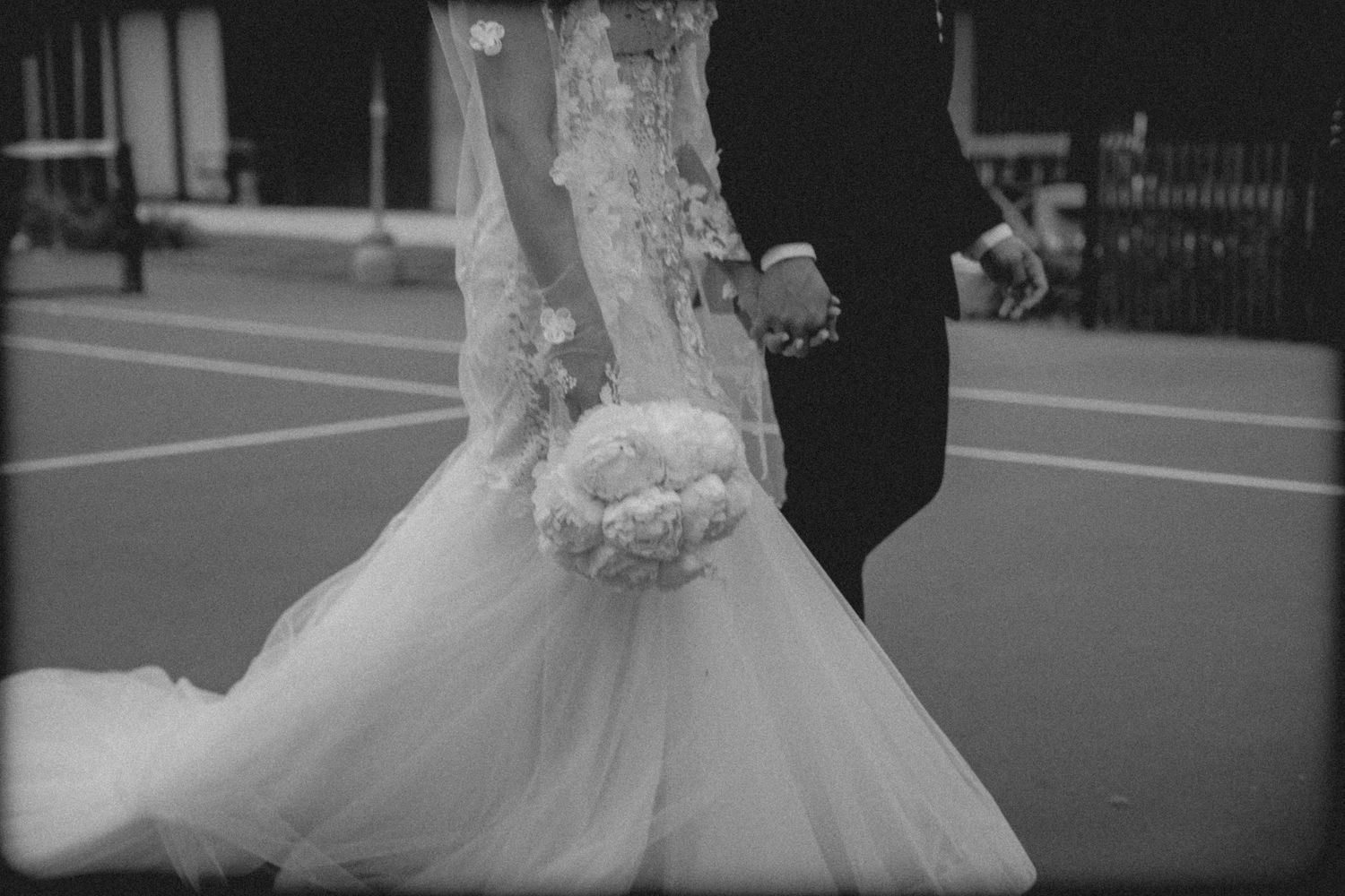 A bride in a white tulle wedding dress walks down a street with her bouquet.