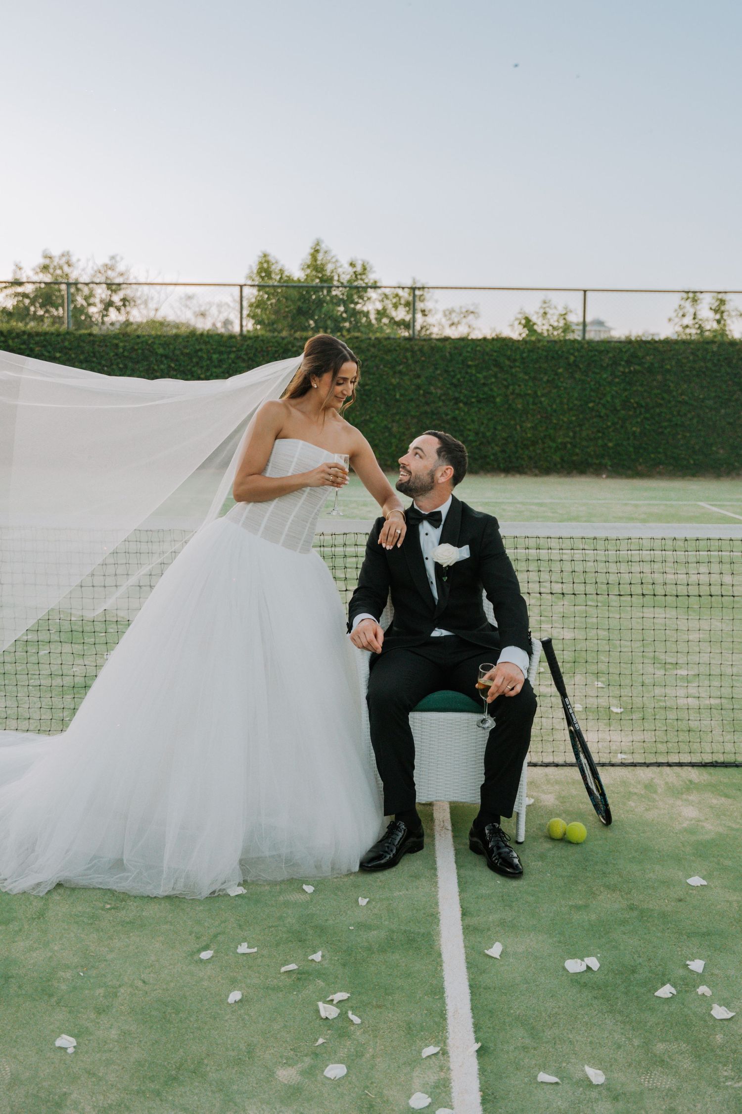 A romantic wedding photo on a tennis court with a flowing white dress and black tuxedo.