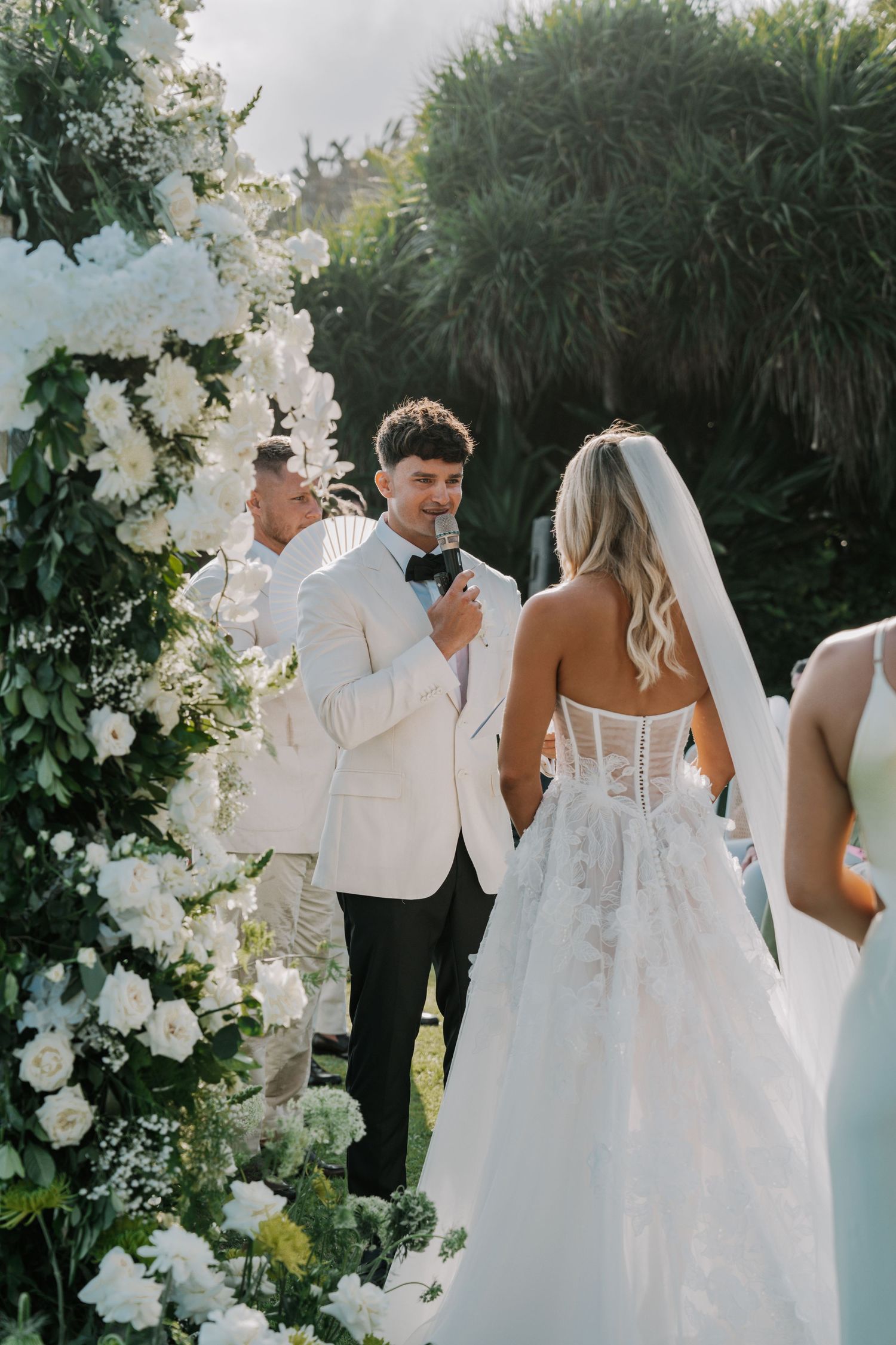 Elegant wedding ceremony setup with white floral arch and decorations in an outdoor garden setting.