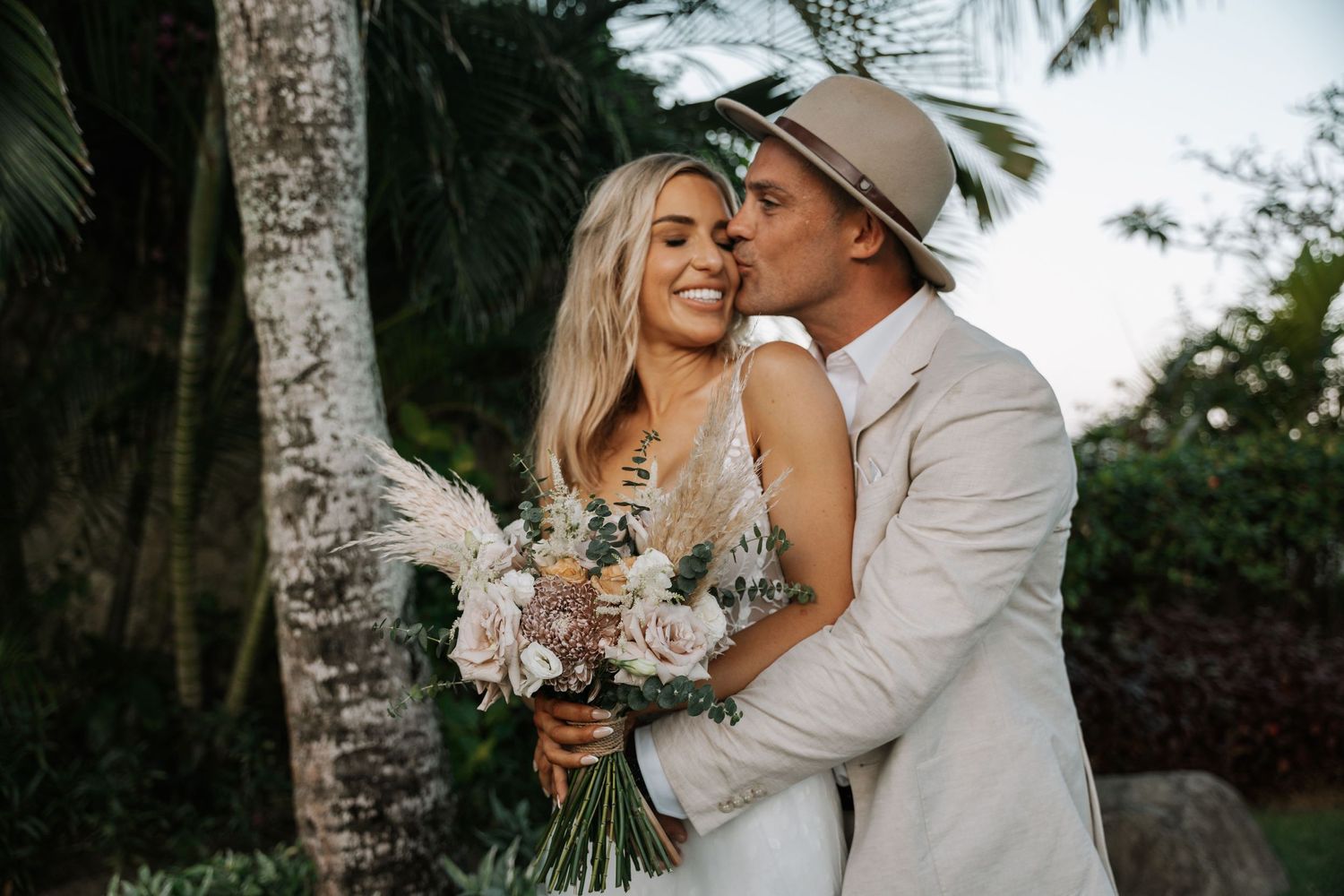 Couple sharing intimate moment in tropical garden setting with soft natural lighting.