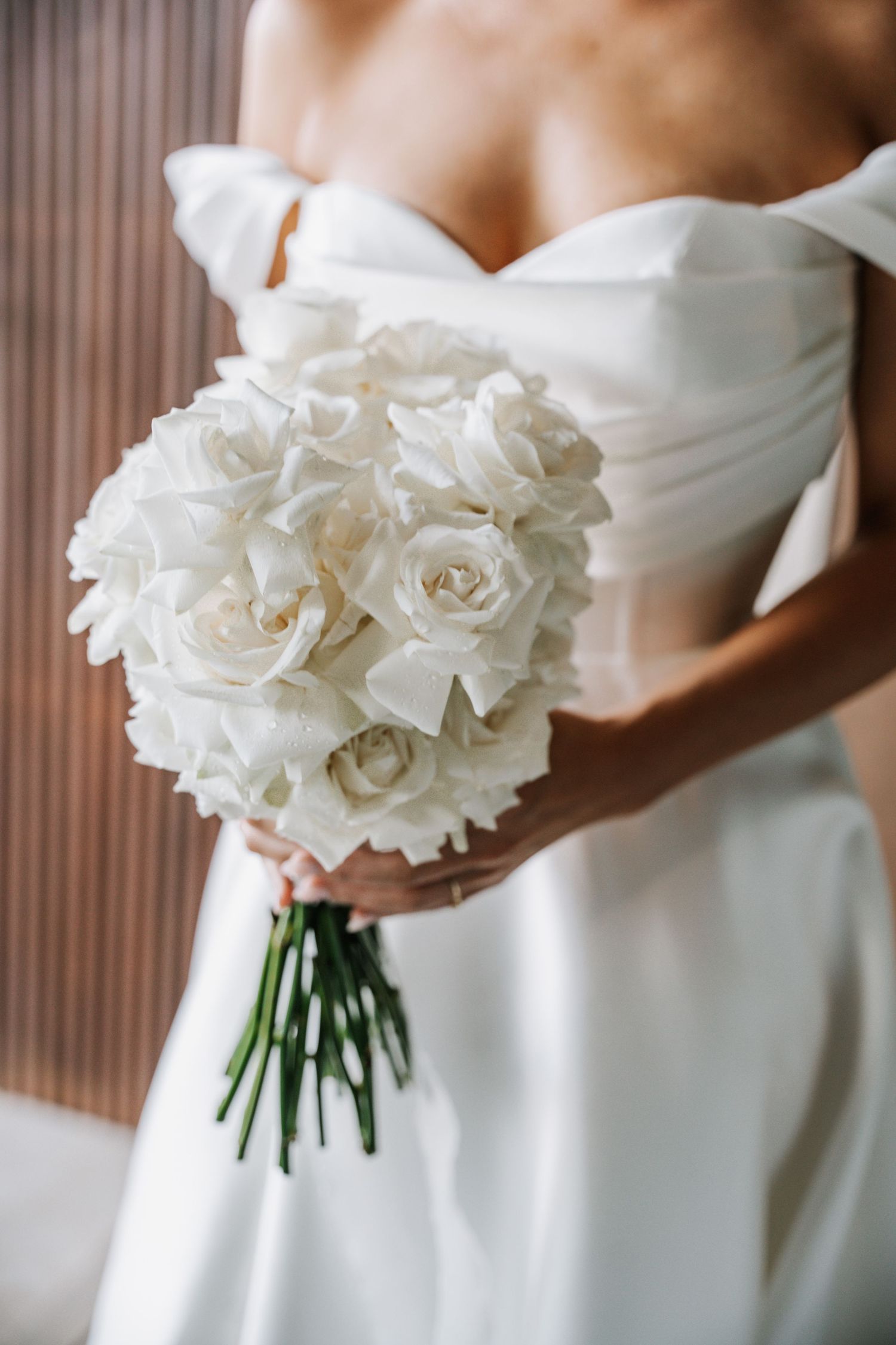 Close-up view of an elegant white rose wedding bouquet against a textured brown background.