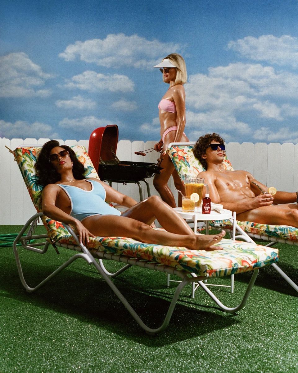 People relaxing on lounge chairs under a blue sky on artificial turf during a sunny summer day.