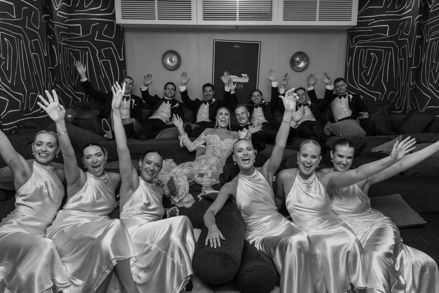 A wedding party in matching white satin robes poses together with raised arms in celebration.