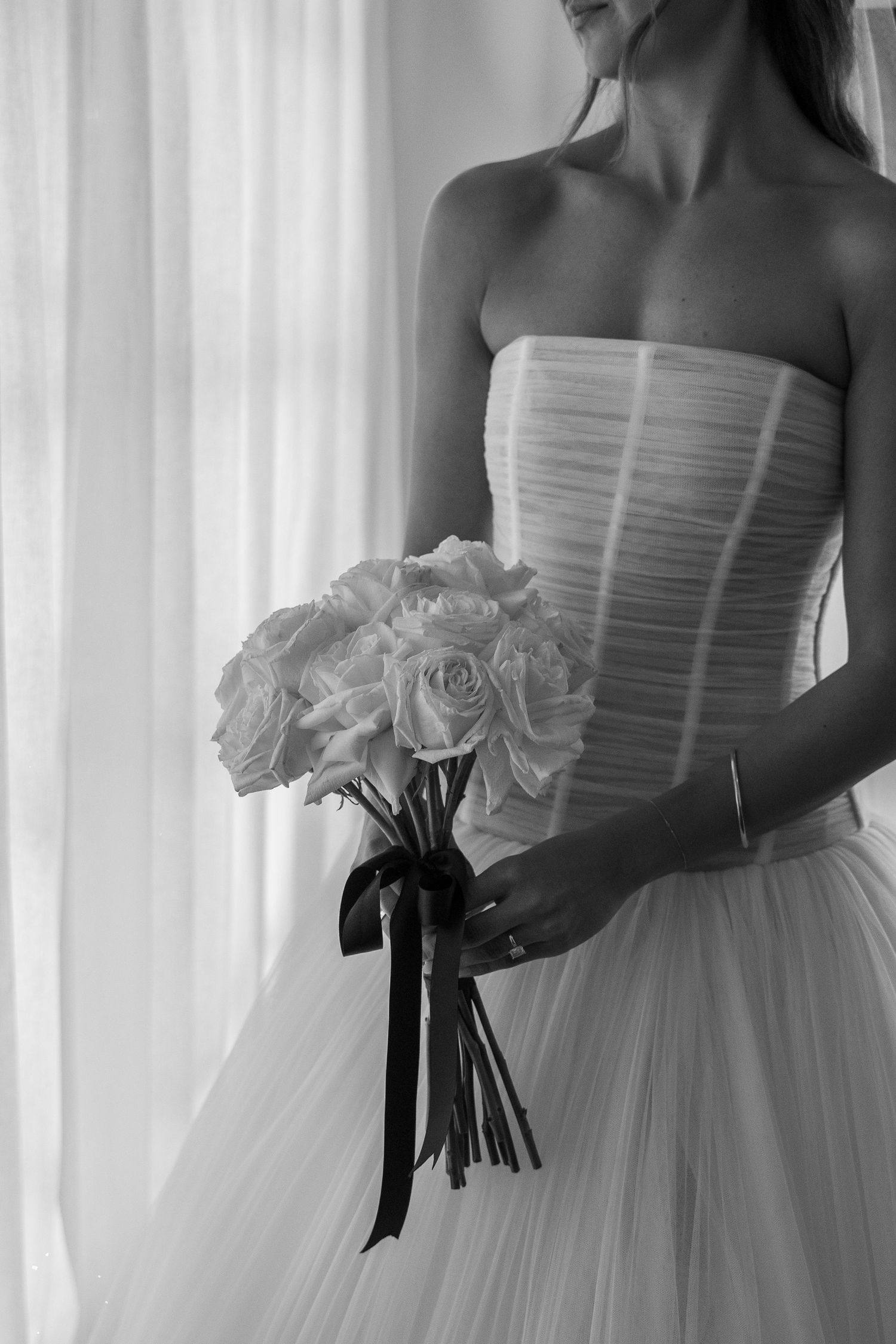 Black and white photo of someone in a strapless wedding dress holding an elegant bouquet of white roses.