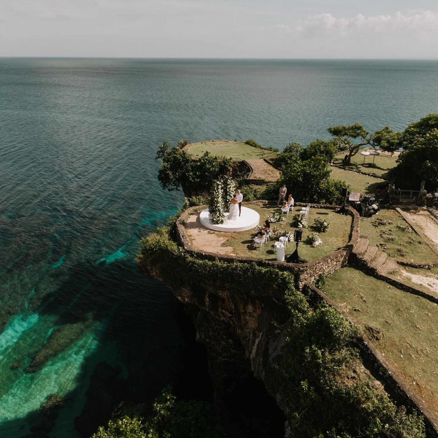 Aerial view of a cliffside wedding ceremony overlooking turquoise ocean waters in Bali, Indonesia.