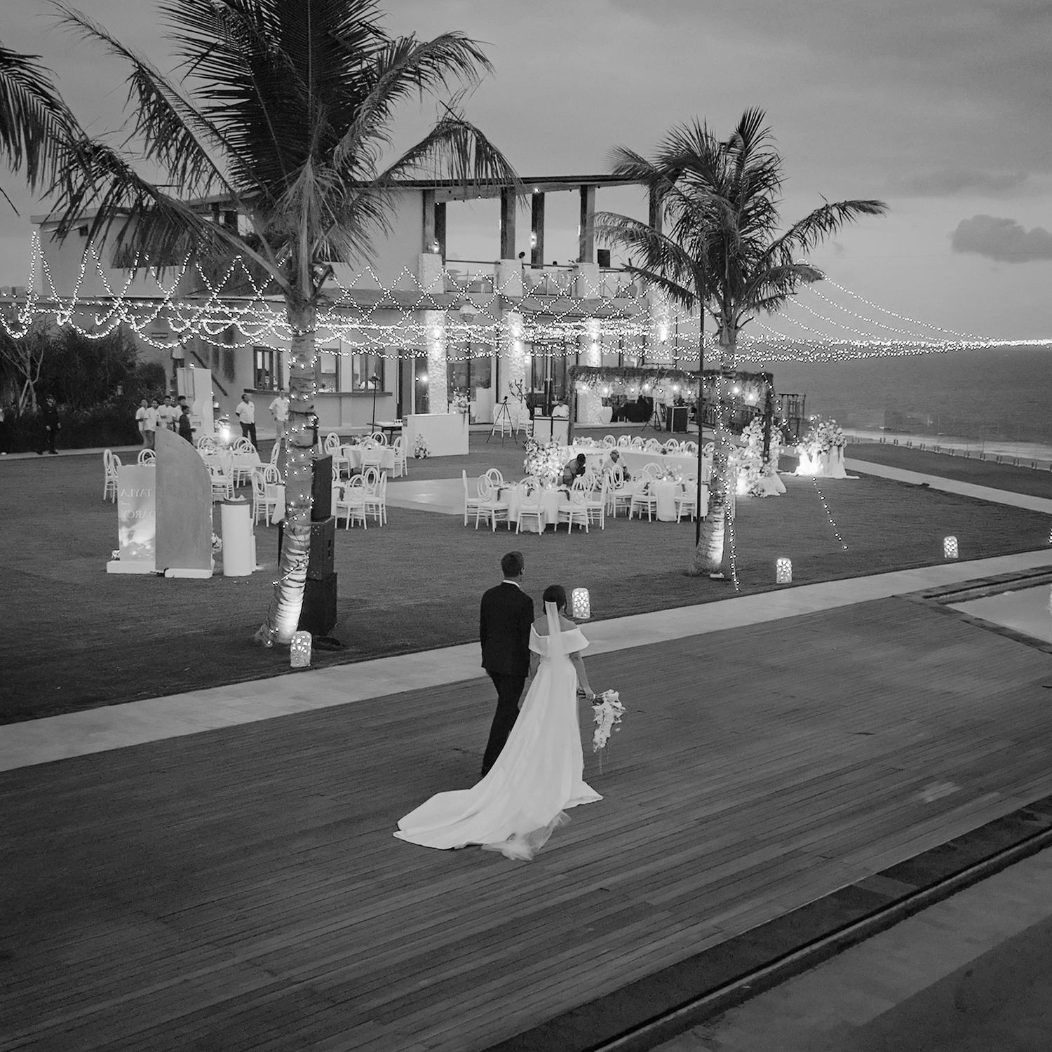 A black and white wedding reception at a beachfront venue with palm trees and elegant outdoor seating arrangements.
