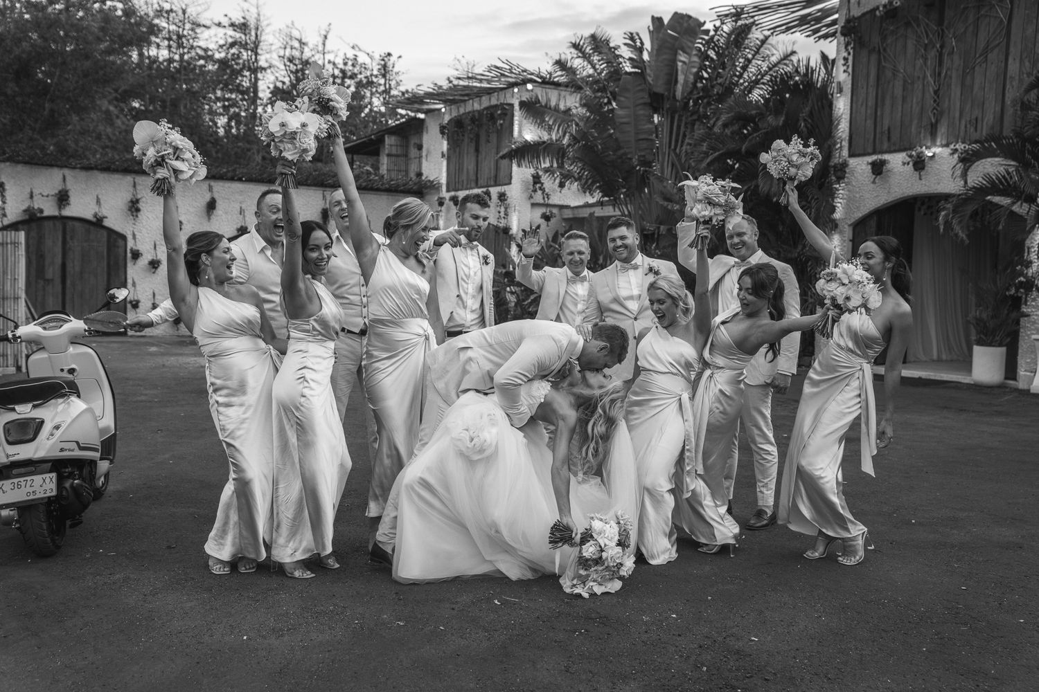Wedding party in white attire poses together on a street in black and white photography.