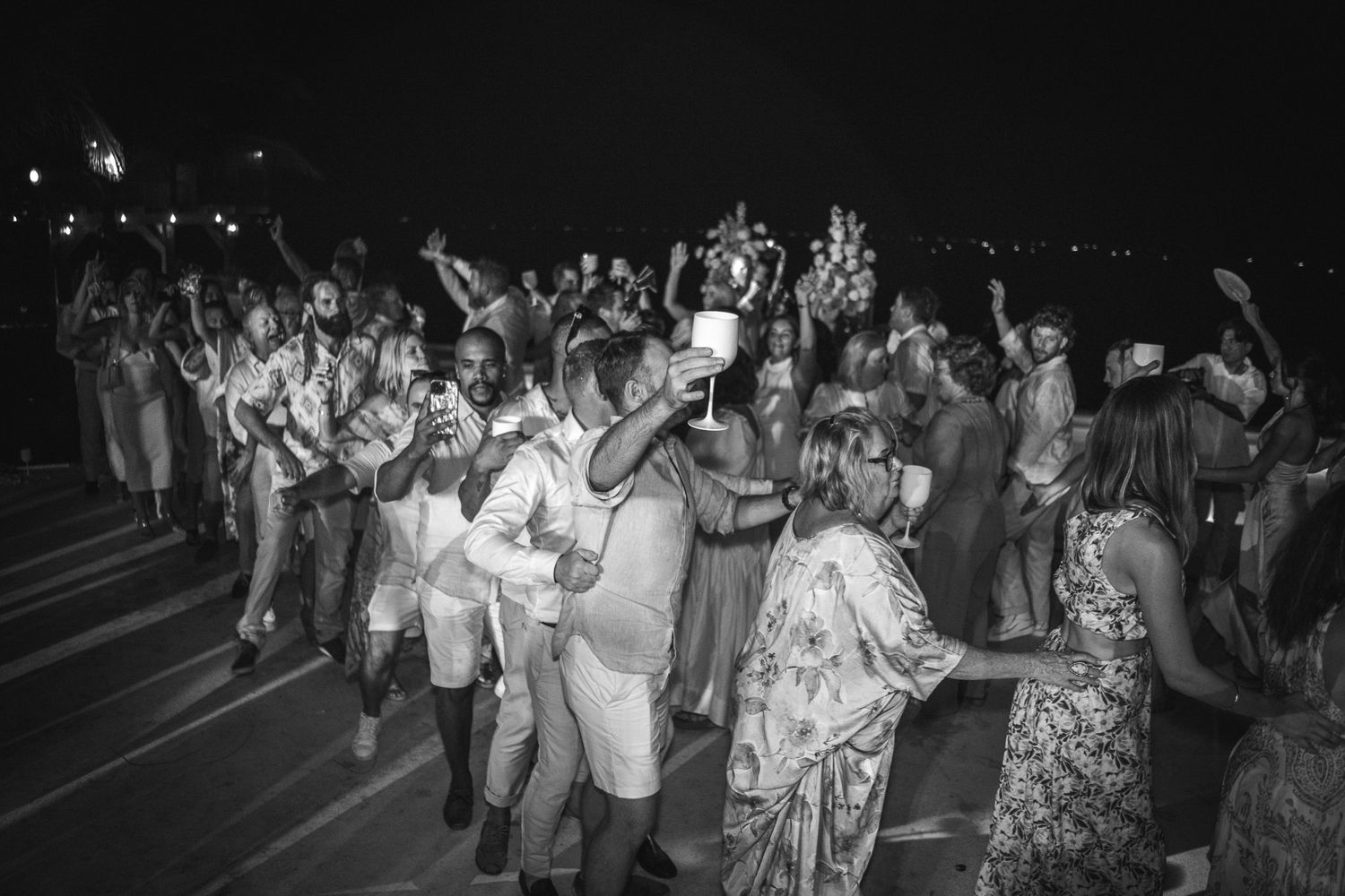 Large crowd of wedding guests dancing and mingling at an outdoor nighttime reception.
