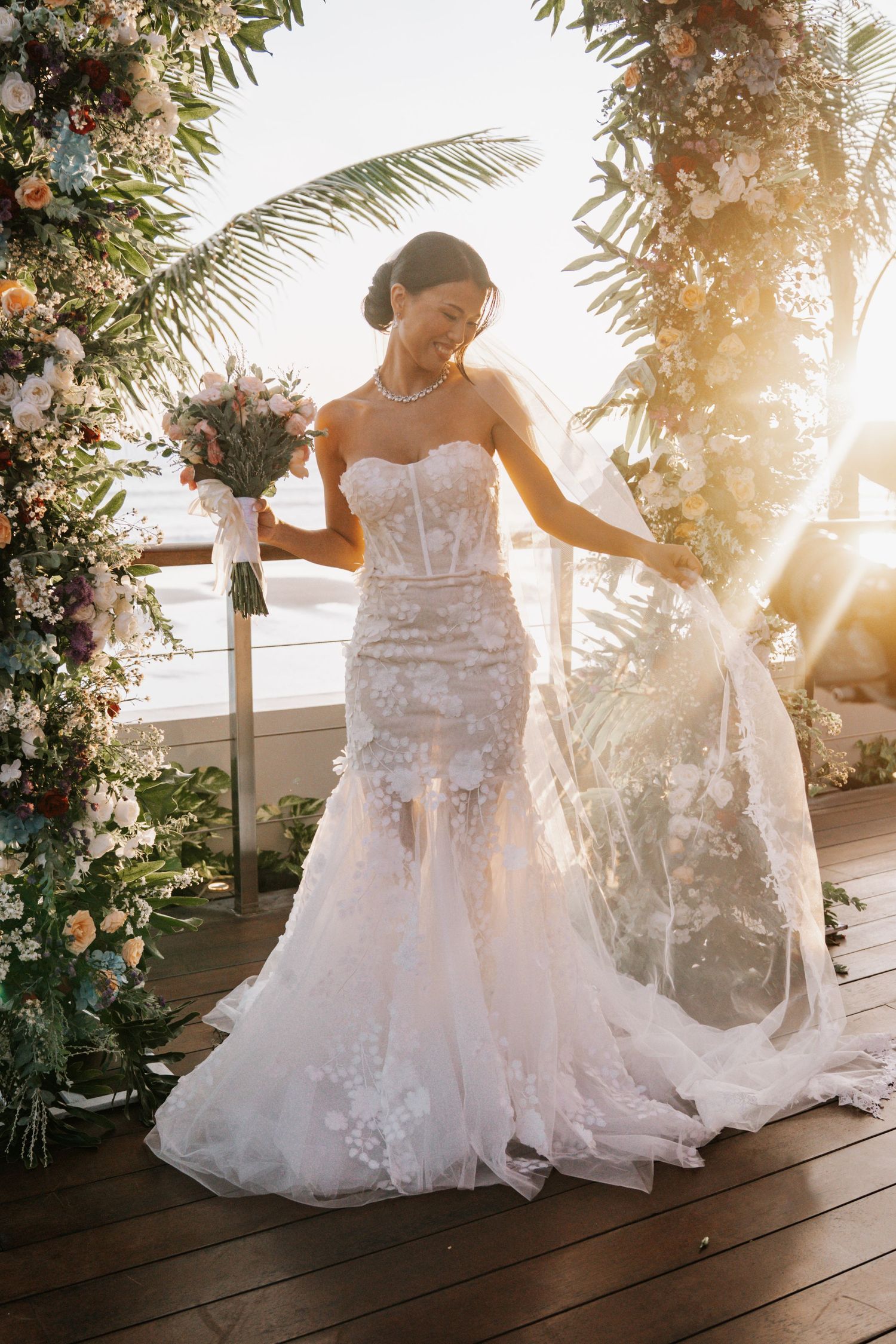 Beautiful lace wedding dress with fitted bodice and flowing train captured at sunset with tropical flowers and palm trees.