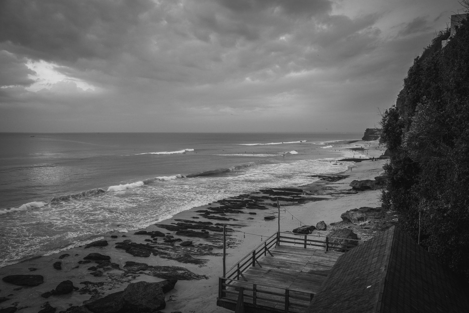 Dramatic black and white coastal landscape with rocky cliffs and crashing waves against a moody sky.