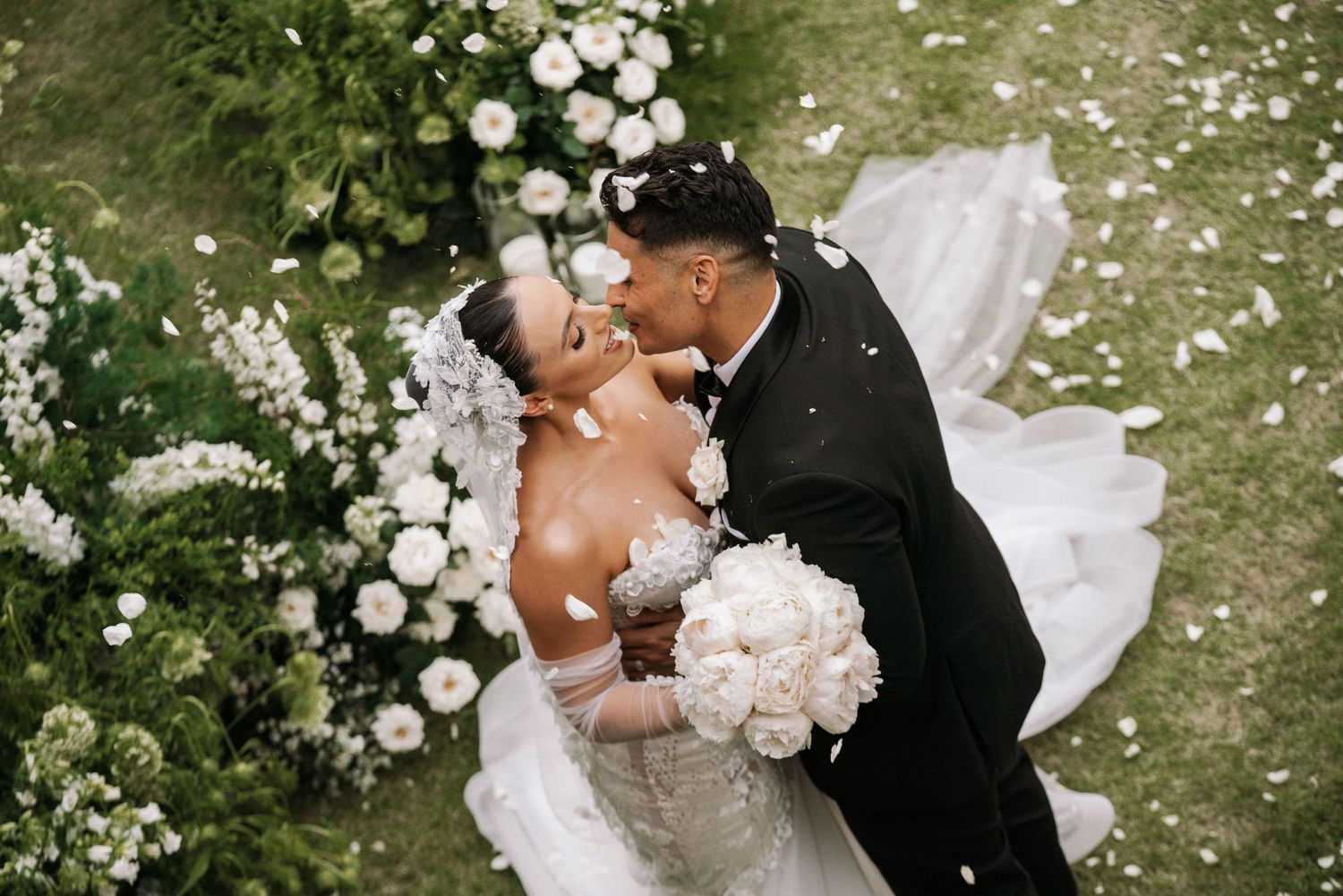 Wedding couple sharing kiss among white flower petals and garden decorations.