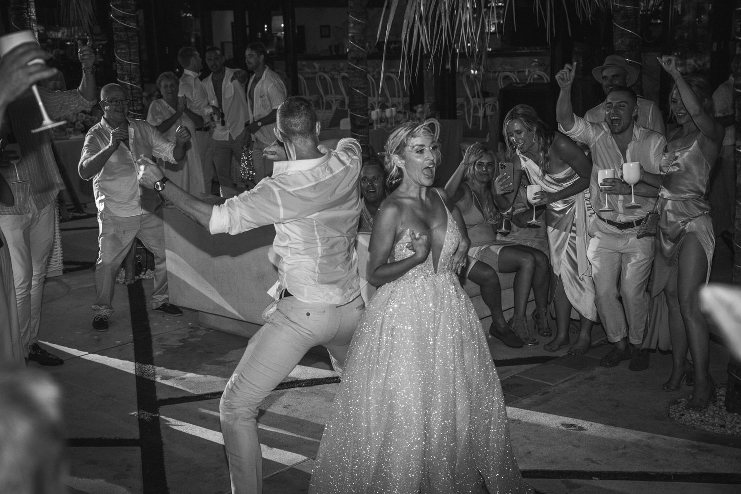 Wedding guests dance together on a crowded dance floor during an evening reception celebration.