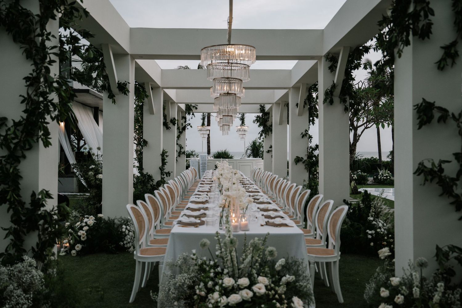 Elegant wedding reception table setup with crystal chandeliers and greenery in a modern white corridor.