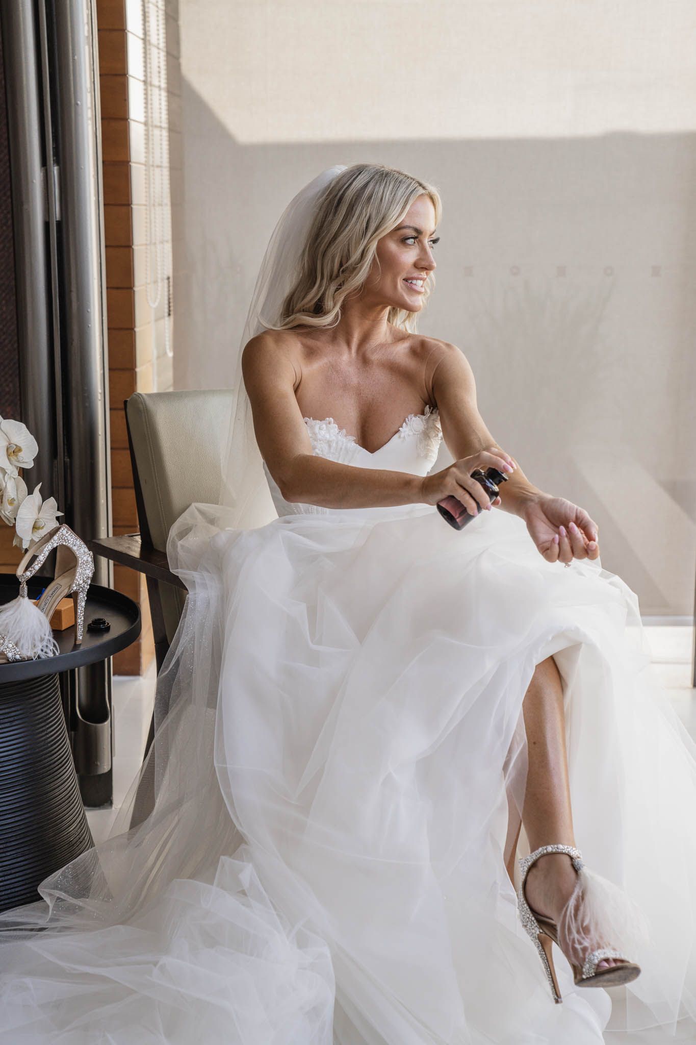 A bride in a flowing white wedding dress poses playfully in an elegant indoor setting with natural light.