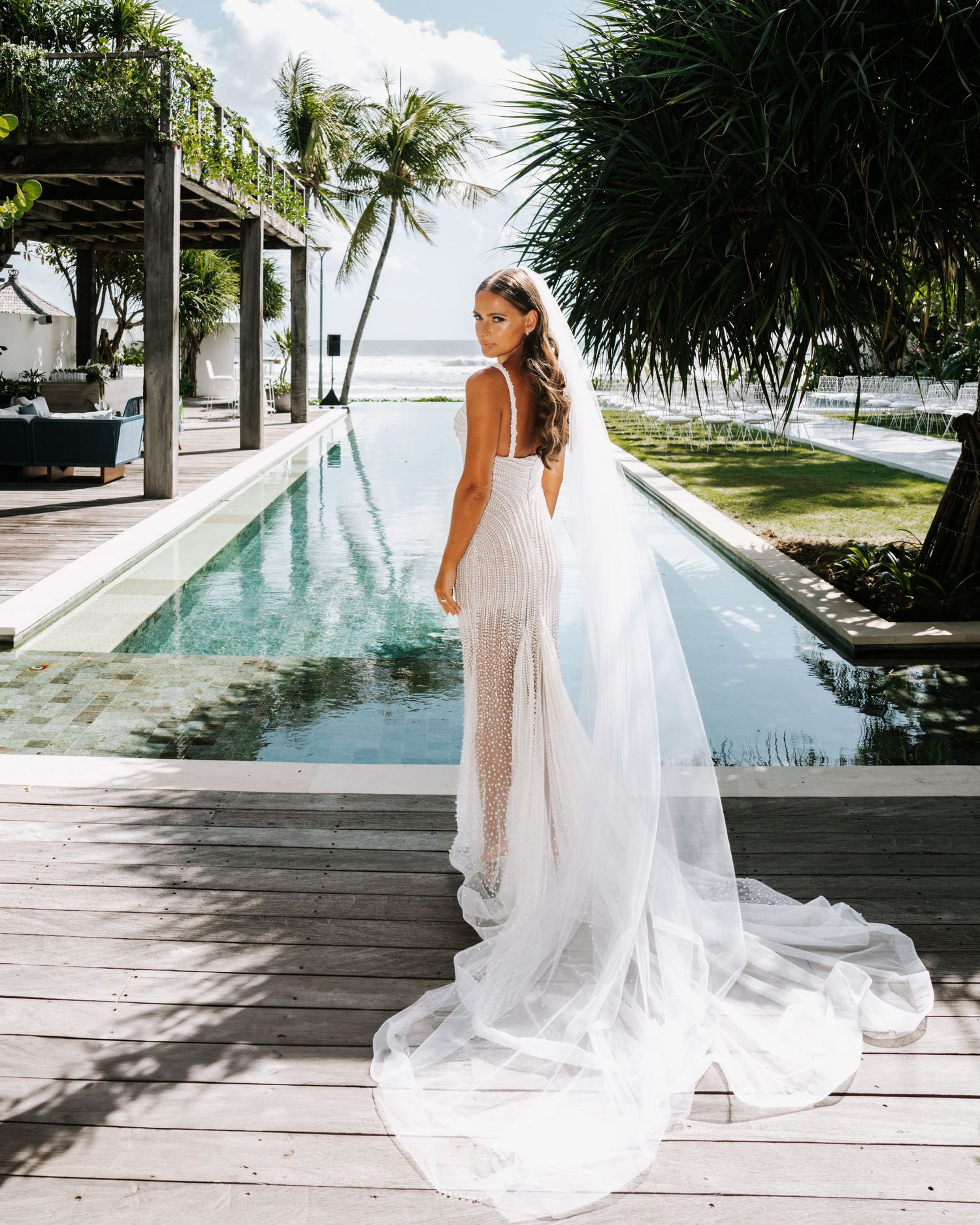 Elegant bridal portrait by infinity pool with ocean and palm trees in background.