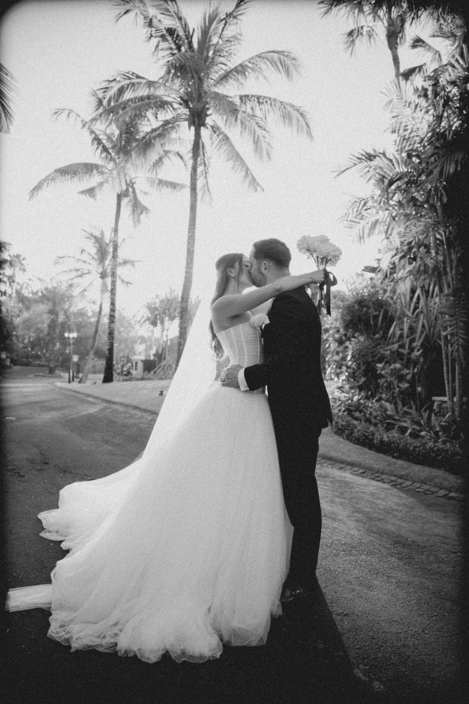 A black and white wedding portrait with palm trees and a flowing white gown.