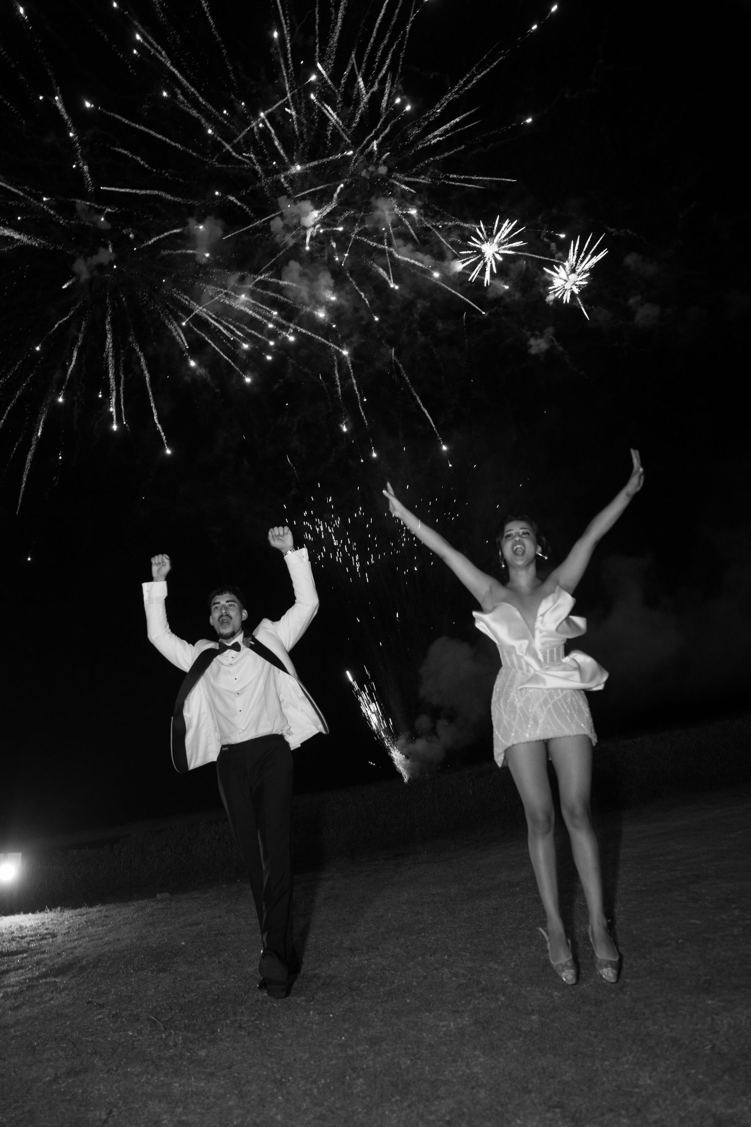 Silhouettes of people dancing and celebrating under fireworks in the night sky during an outdoor celebration.