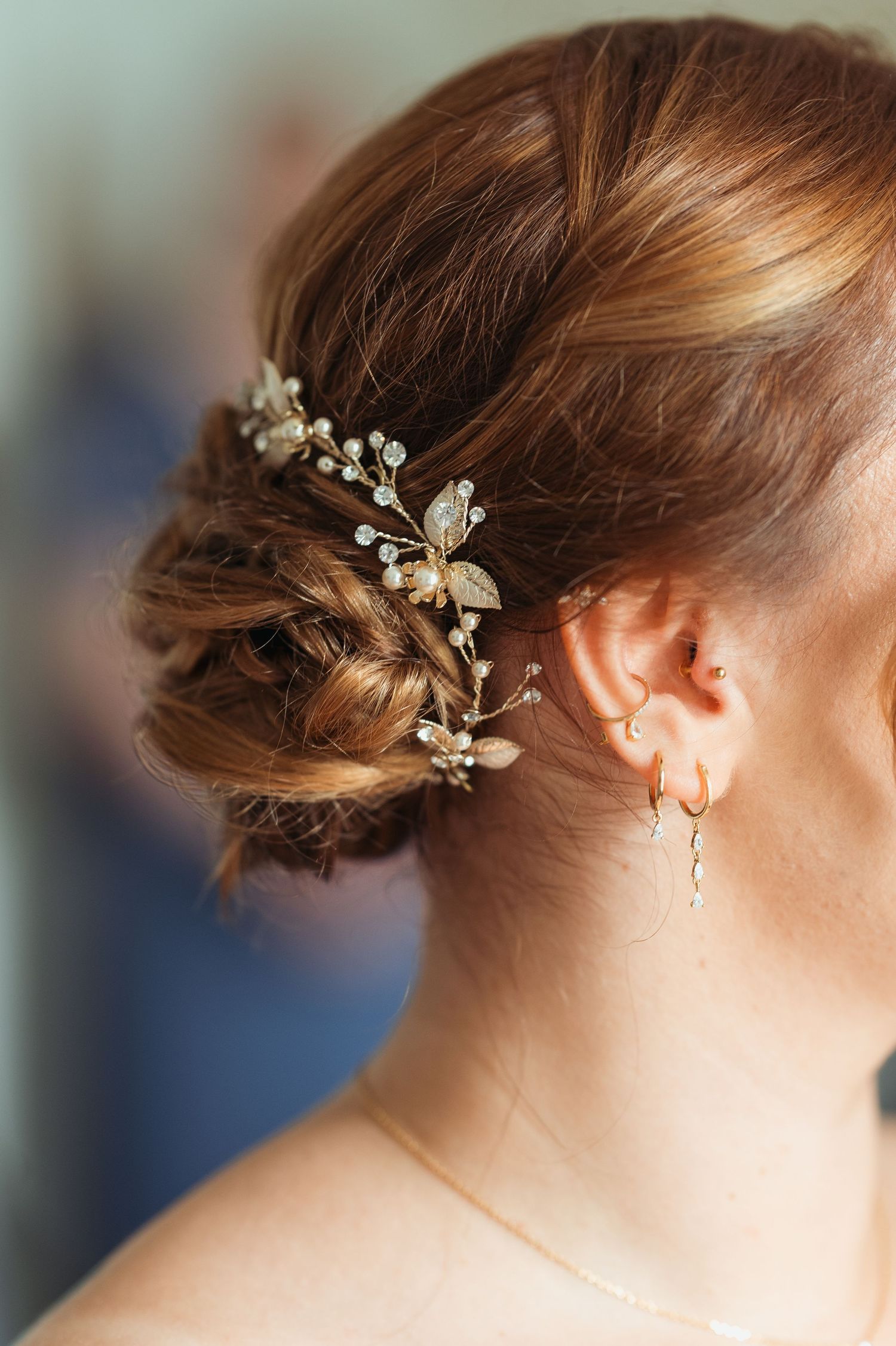 Close-up of bride's elegant updo hairstyle adorned with a delicate gold floral hair vine and pearl accessories.
