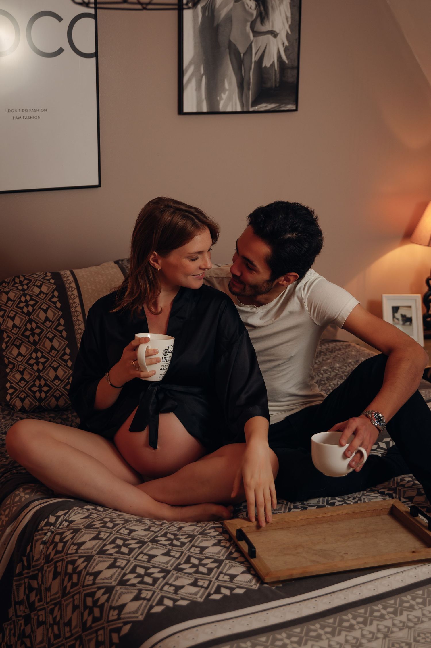 Expecting couple relaxing together on a cozy bed with coffee mugs.