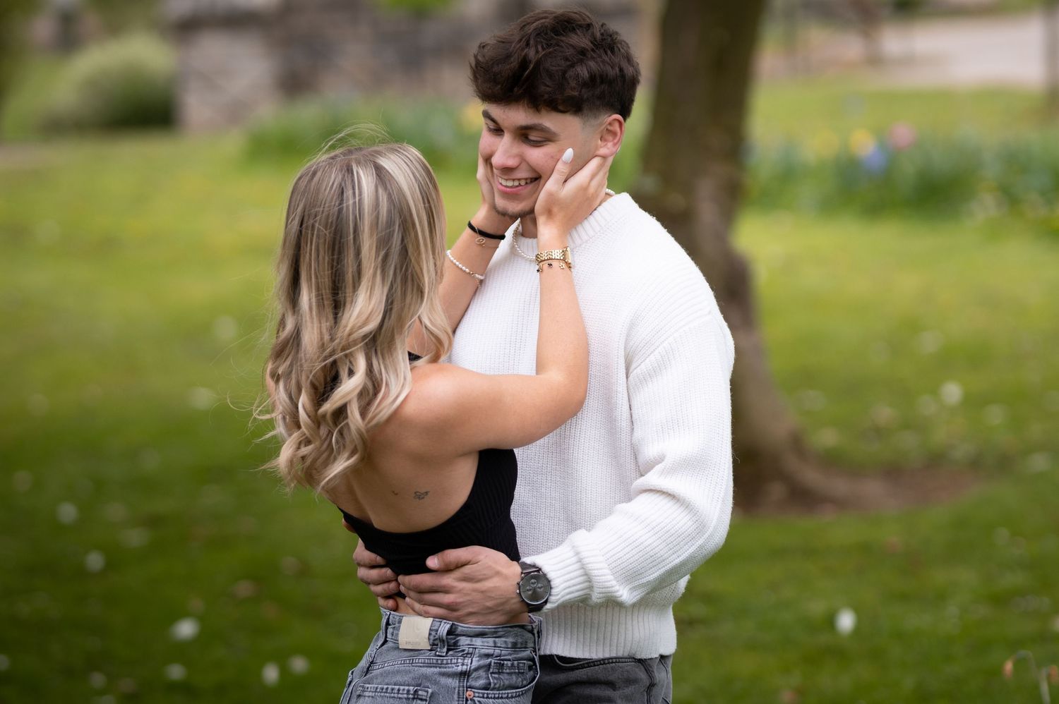 Young couple sharing tender romantic moment embracing in blooming spring garden during photo session.