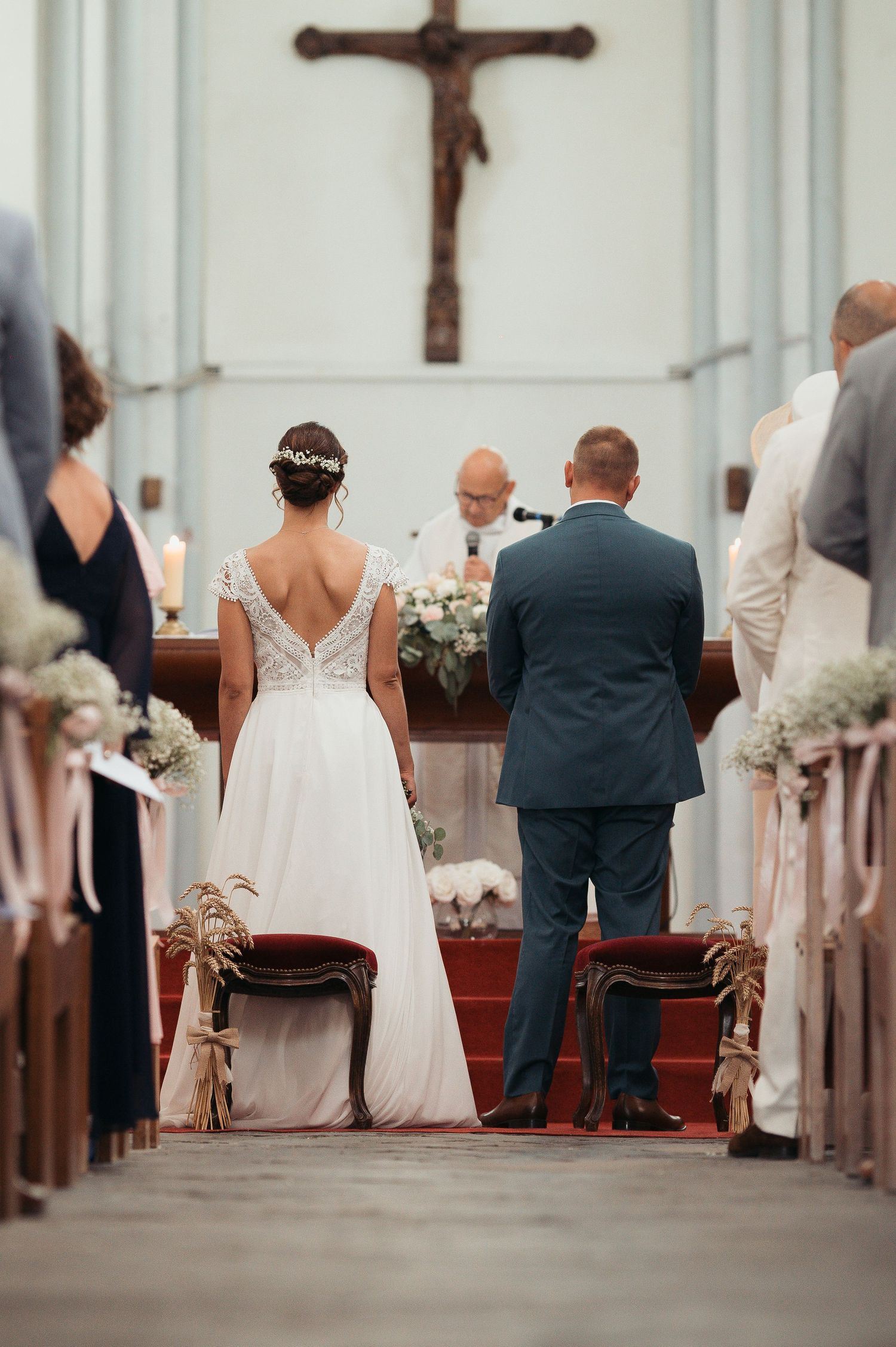 Bride and groom stand at church altar during wedding ceremony with crucifix and officiant in background.