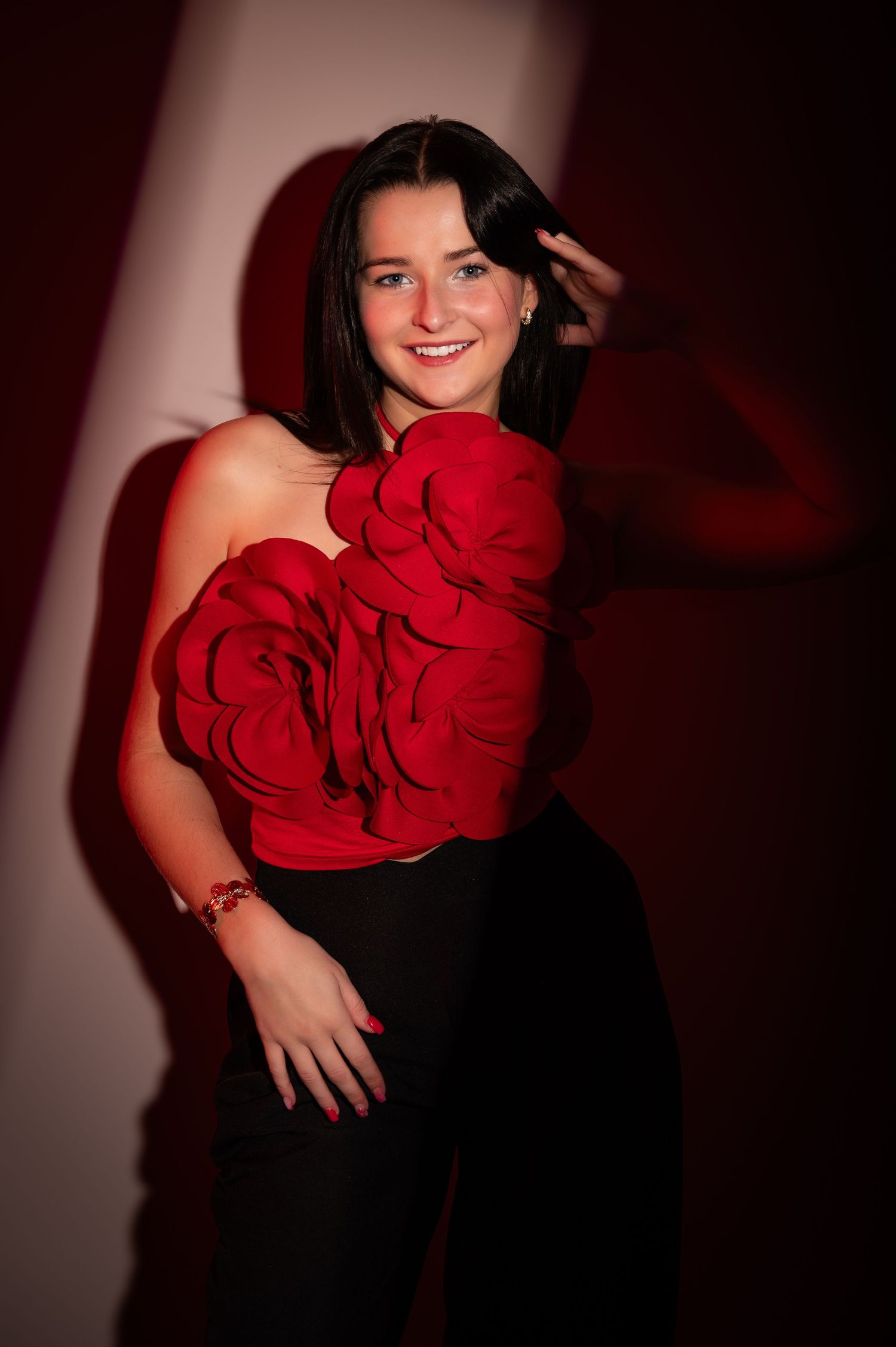 Woman in red floral strapless top and black pants posing confidently against a dramatic red-lit background.