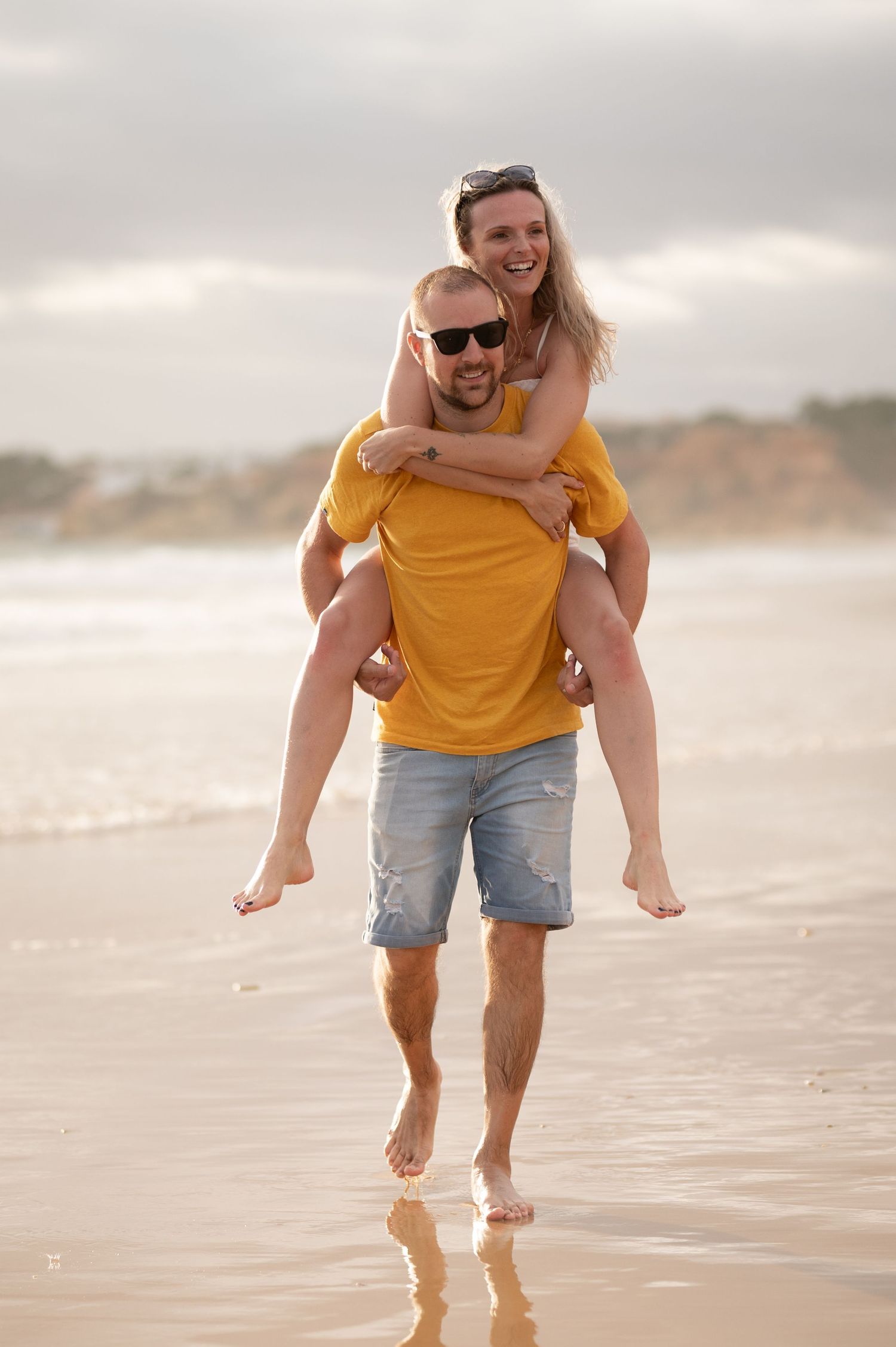 Happy couple enjoying a piggyback ride on a sandy beach at sunset.
