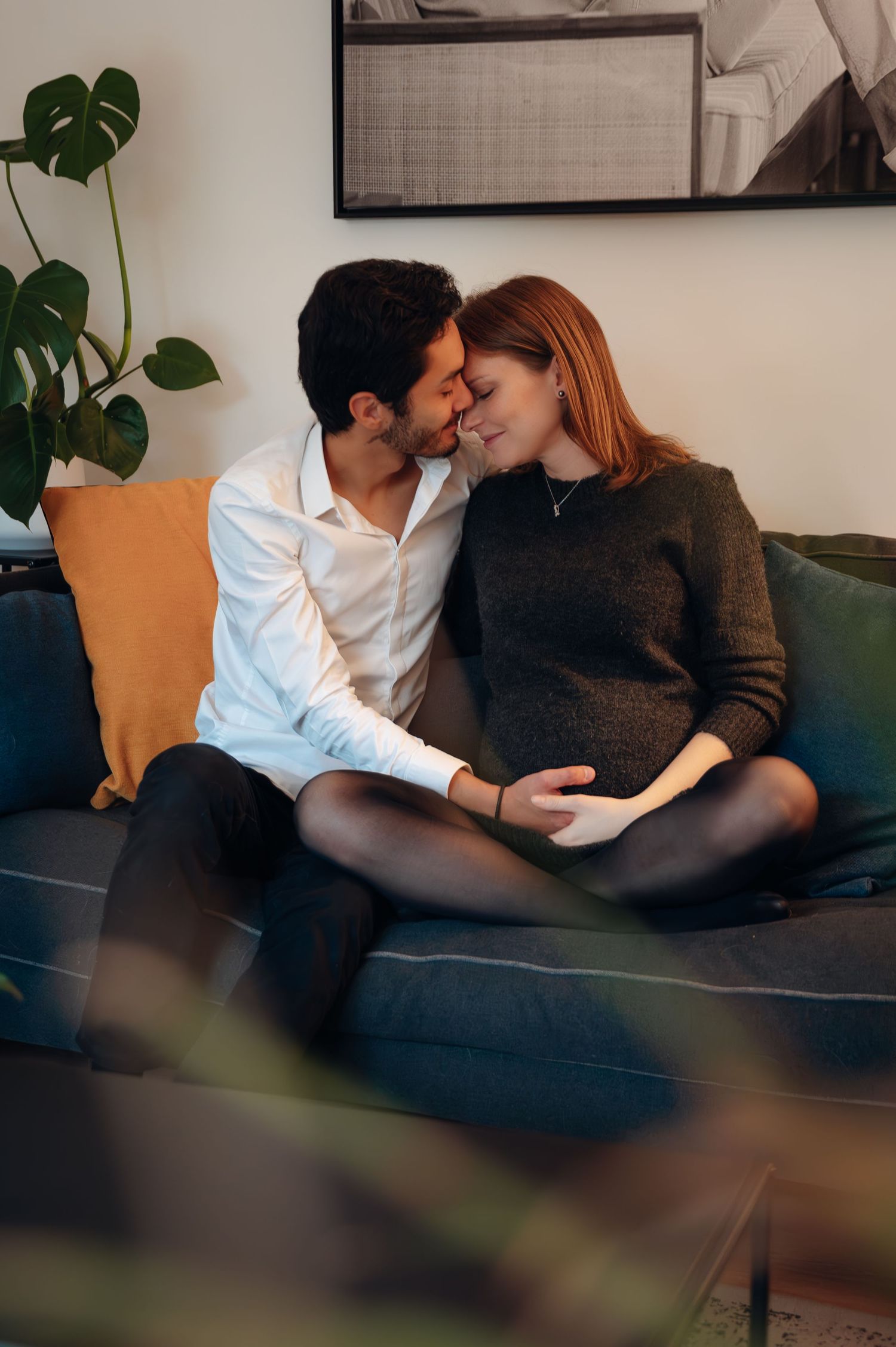 A couple shares a tender moment on a couch, man kissing pregnant woman's cheek while touching her belly.