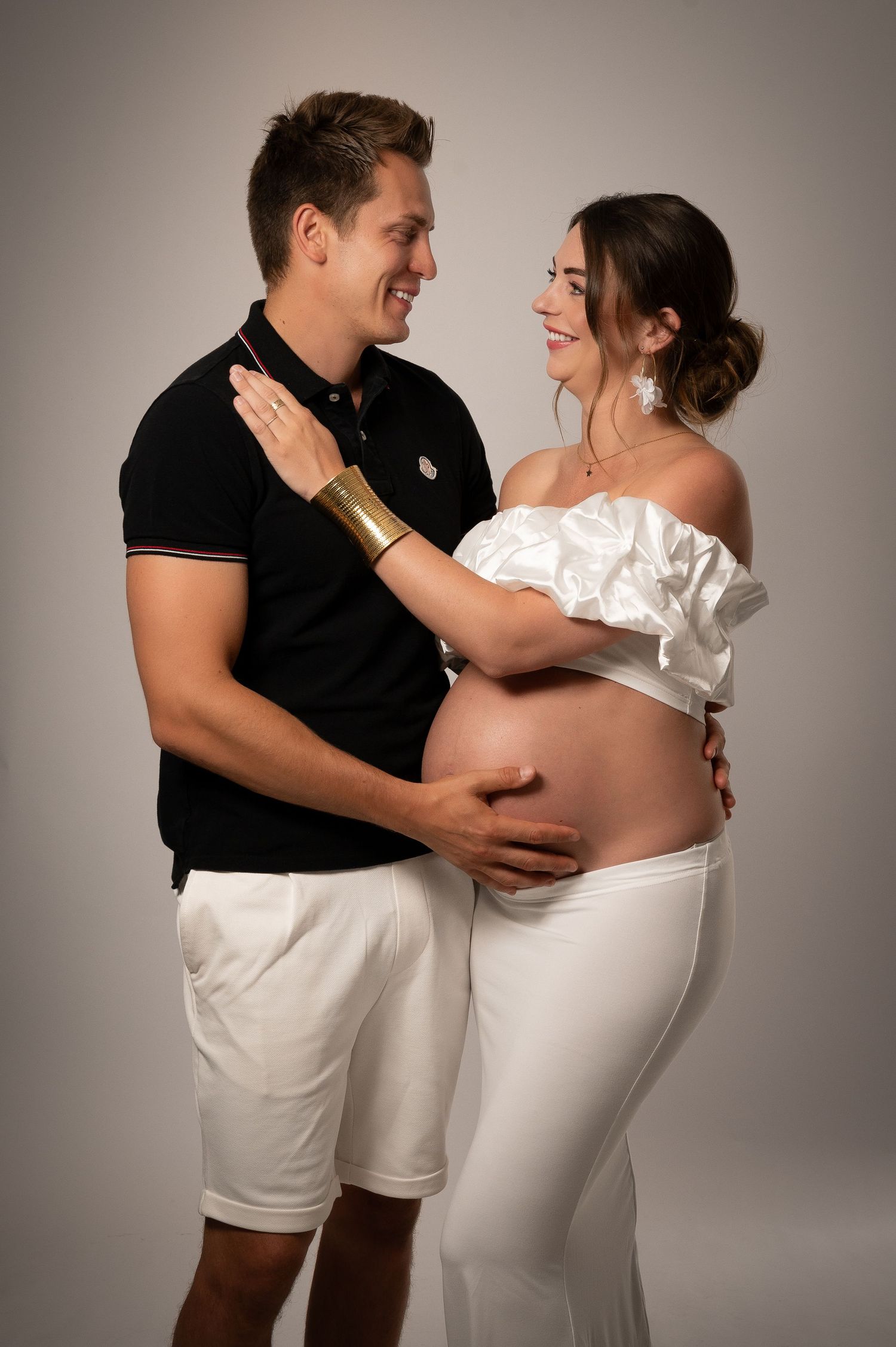 Smiling couple poses for a maternity photo shoot, gently cradling the pregnant womans bare baby bump.