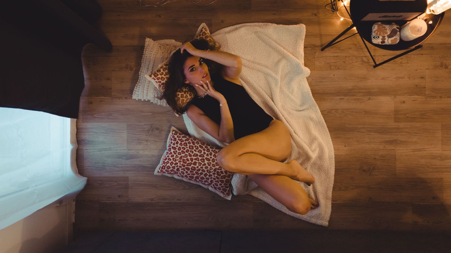 Overhead view of a young woman lying on a white blanket on a wooden floor with leopard print pillows.