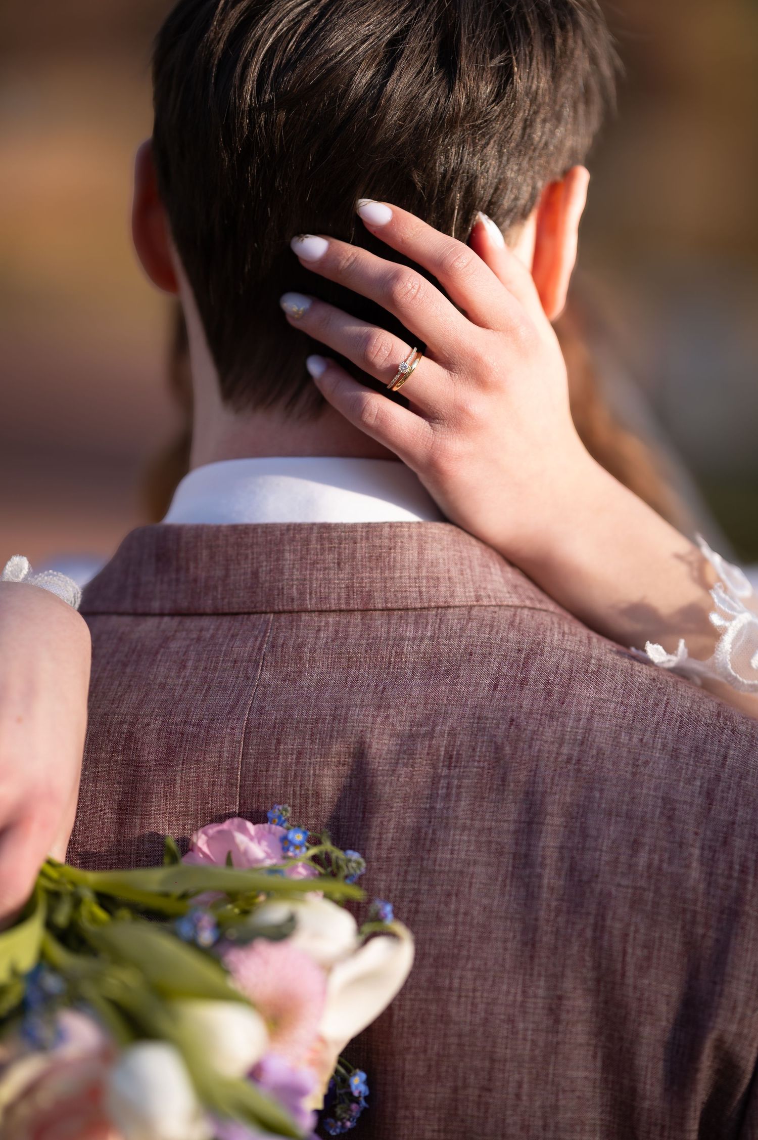 Bride placing hand on grooms neck showing engagement ring while holding a floral bouquet.