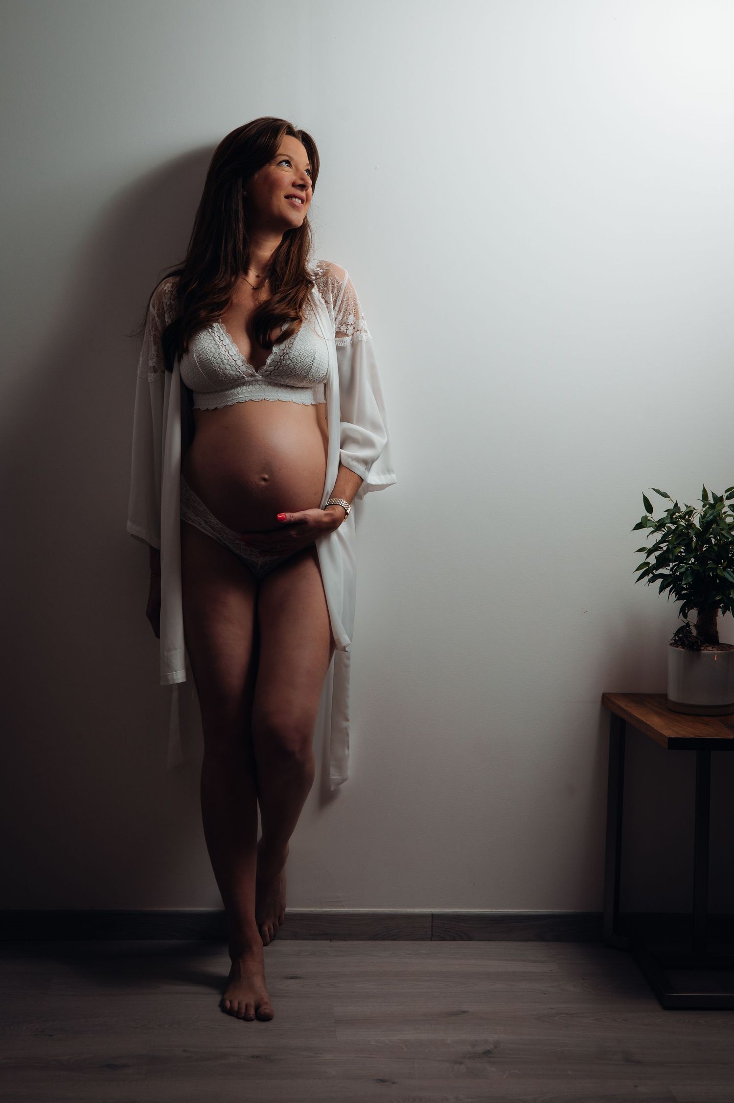 Une future maman sublime en lingerie blanche et peignoir, capturée dans un intérieur épuré et doux, avec une touche naturelle