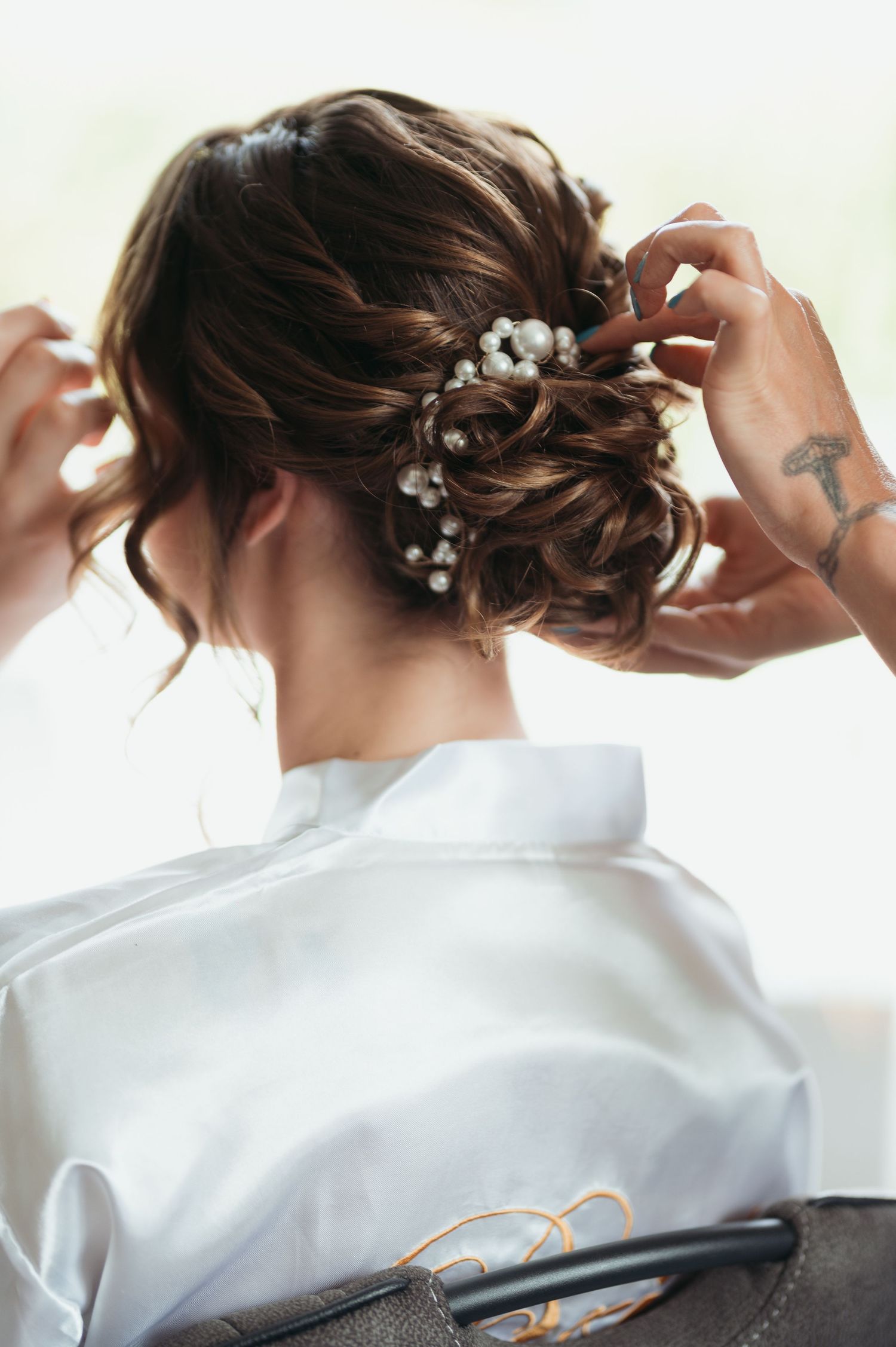 Woman with elegant bridal updo hairstyle adorned with pearl pins, wearing a white satin robe.