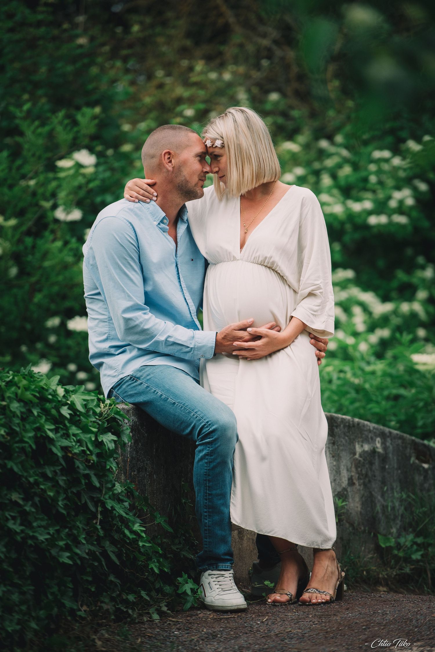 Couple sharing a tender moment during a maternity photoshoot in a lush green garden.