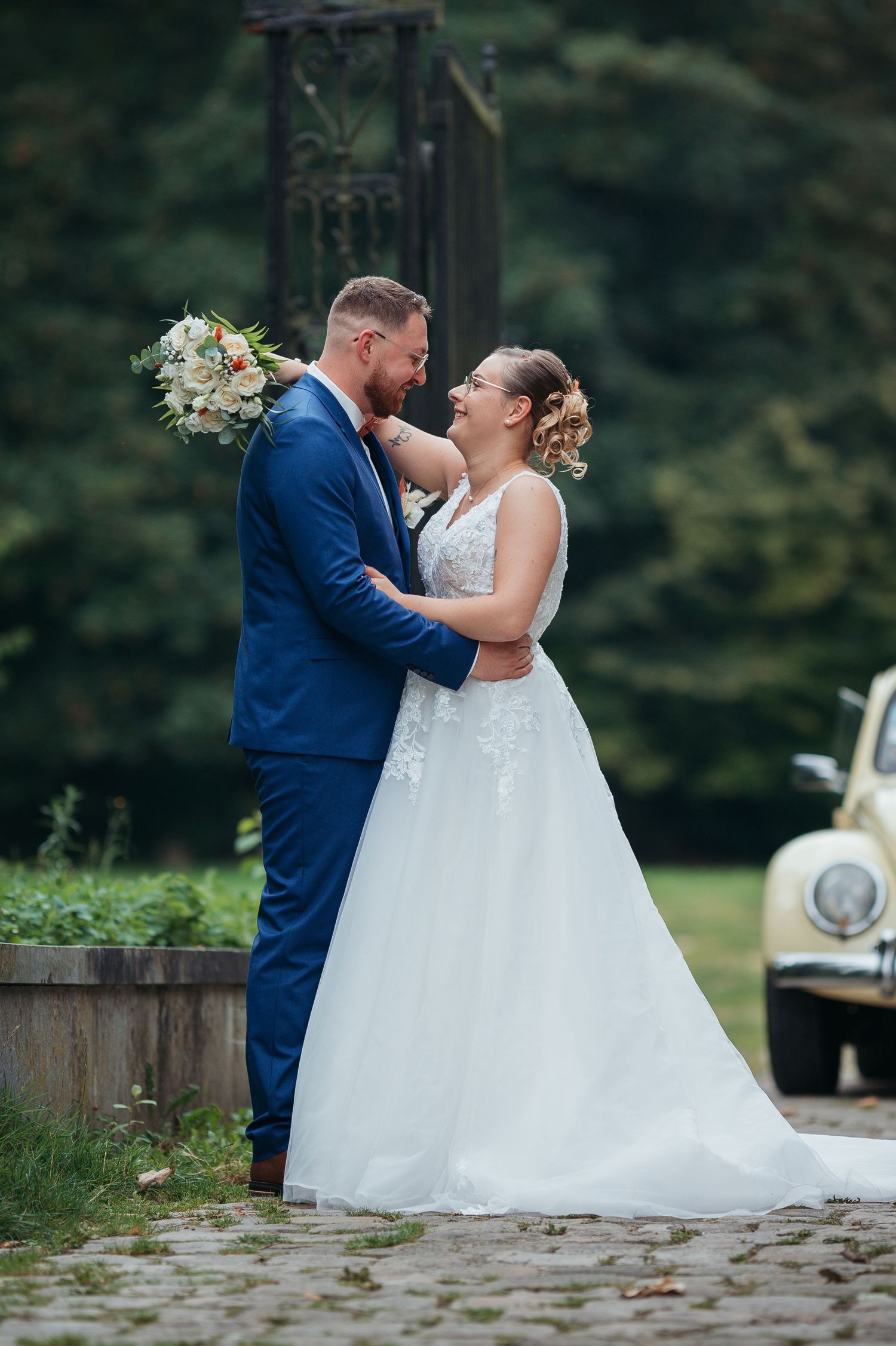 Newlywed couple sharing a romantic moment outdoors with a vintage car backdrop.