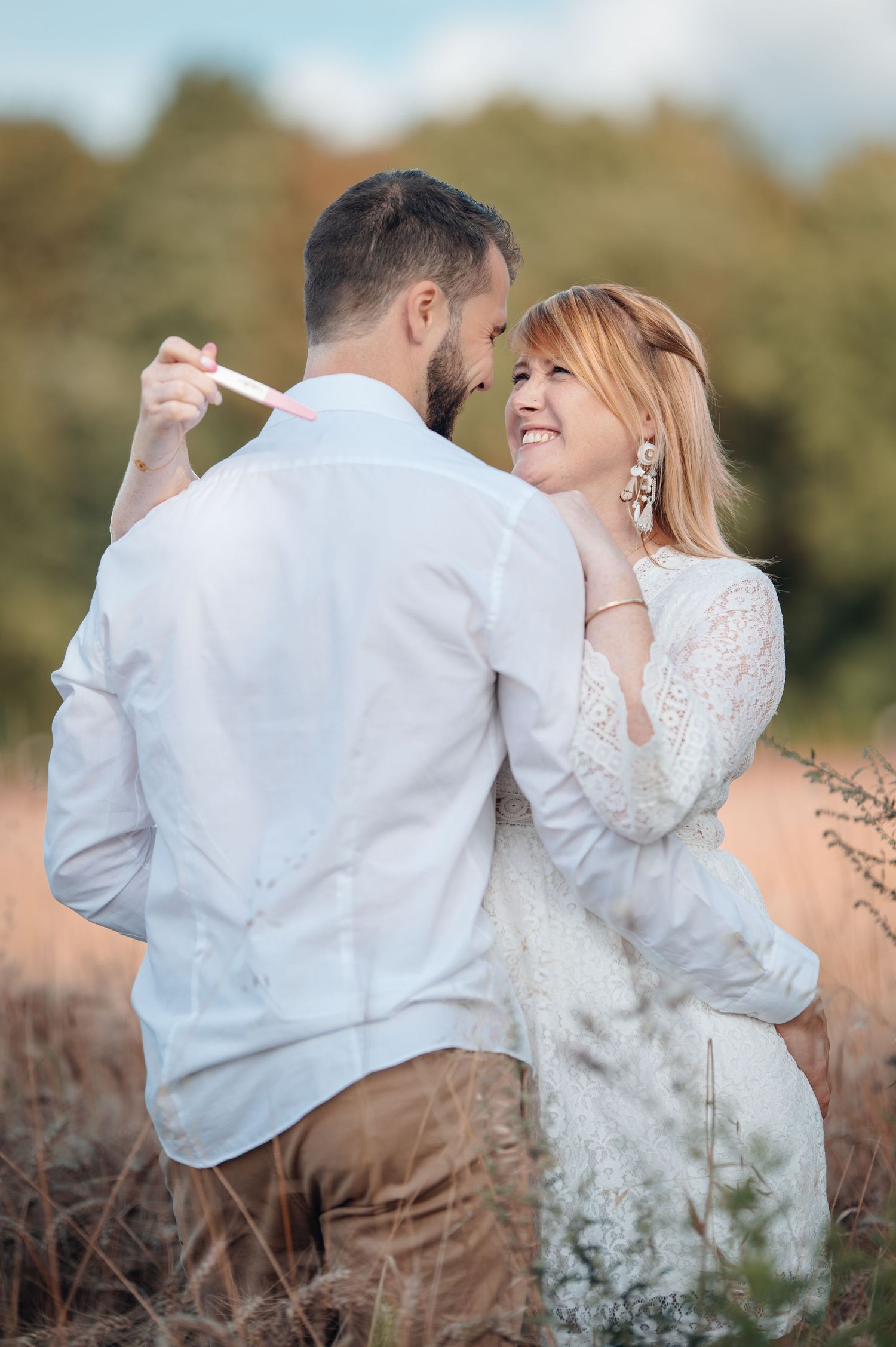 A smiling couple dances romantically in a golden field, the woman in white lace gazing up at her partner.