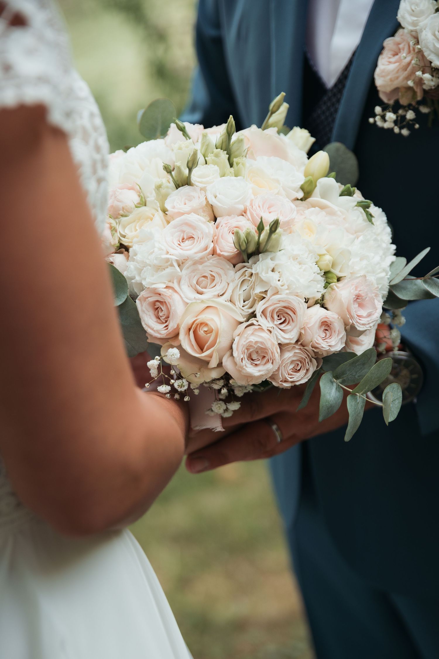 Bride and groom holding a romantic blush pink and white rose wedding bouquet with eucalyptus greenery.