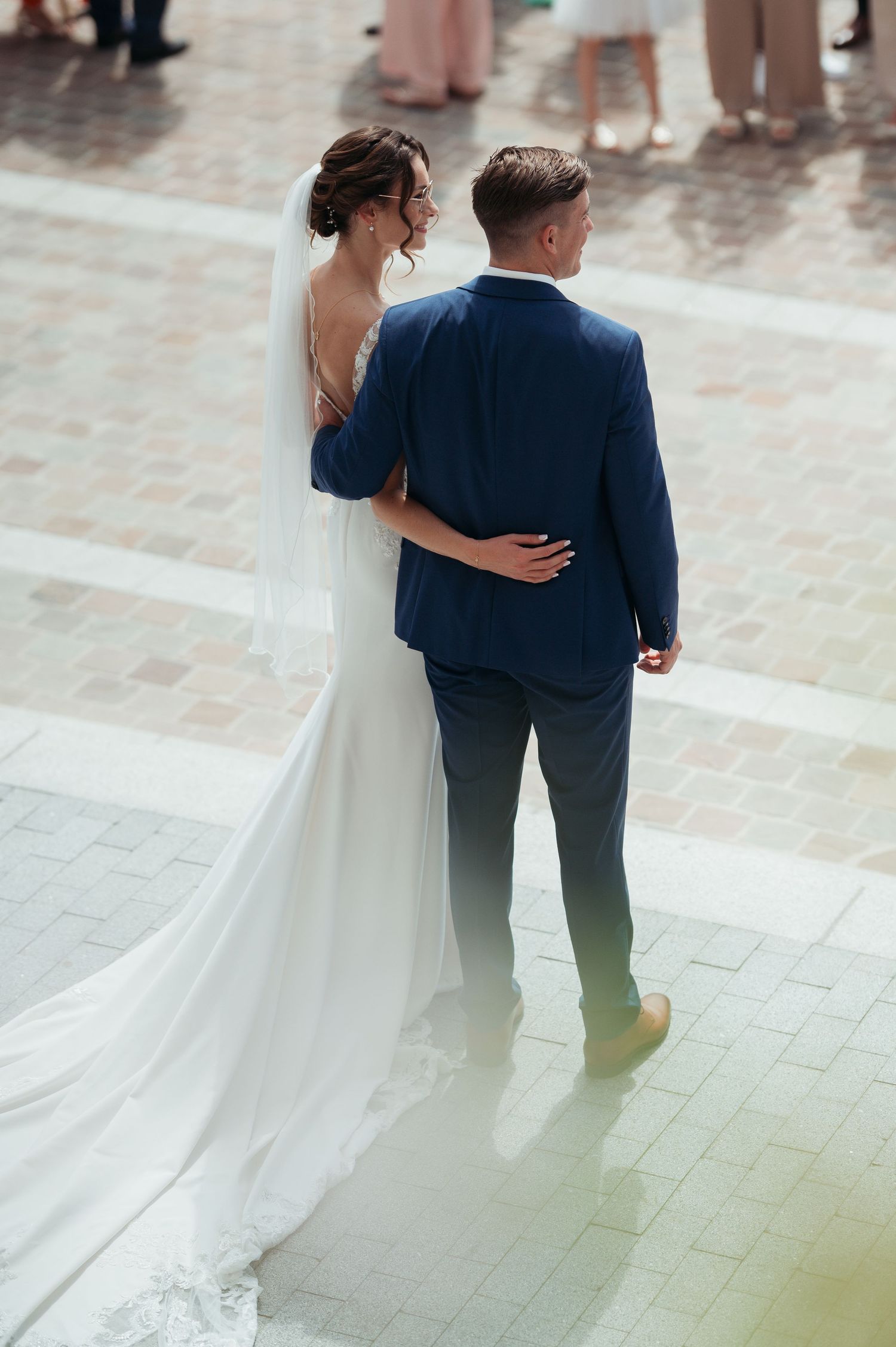 Bride in white gown and groom in navy suit walk together arm in arm at outdoor wedding ceremony.