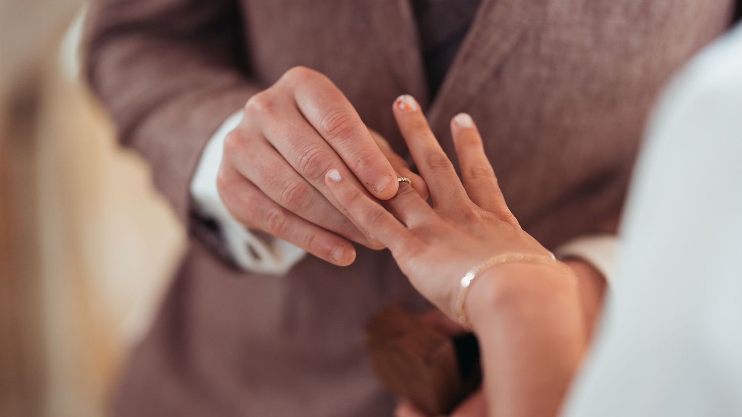 Close-up of groom placing a gold wedding ring on bride's finger during a wedding ceremony.