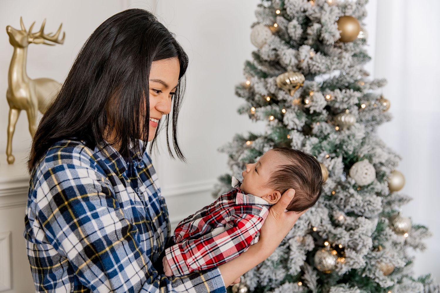 Baby's first Christmas, a newborn with their mom exchange smiles with a Christmas tree in the background.