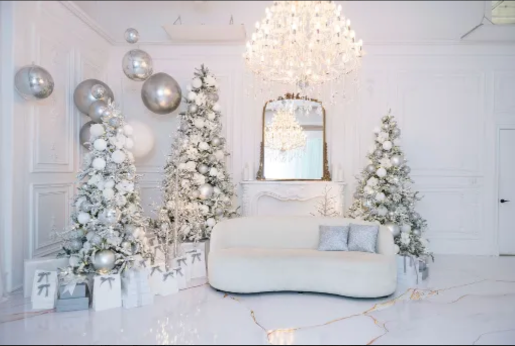 Winter wonderland holiday set up with three flocked white Christmas trees, white couch, and elegant mirror on white walls.