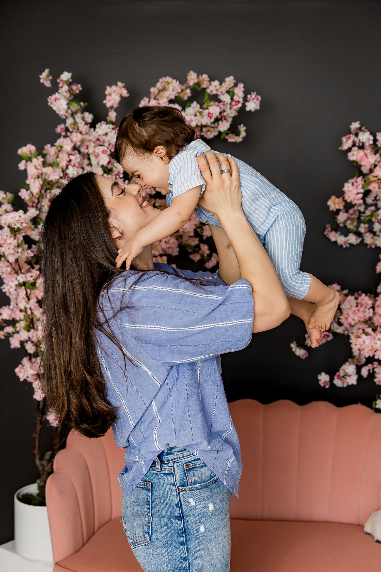 Tender moment between mother and child with pink cherry blossoms decorating a dark background.