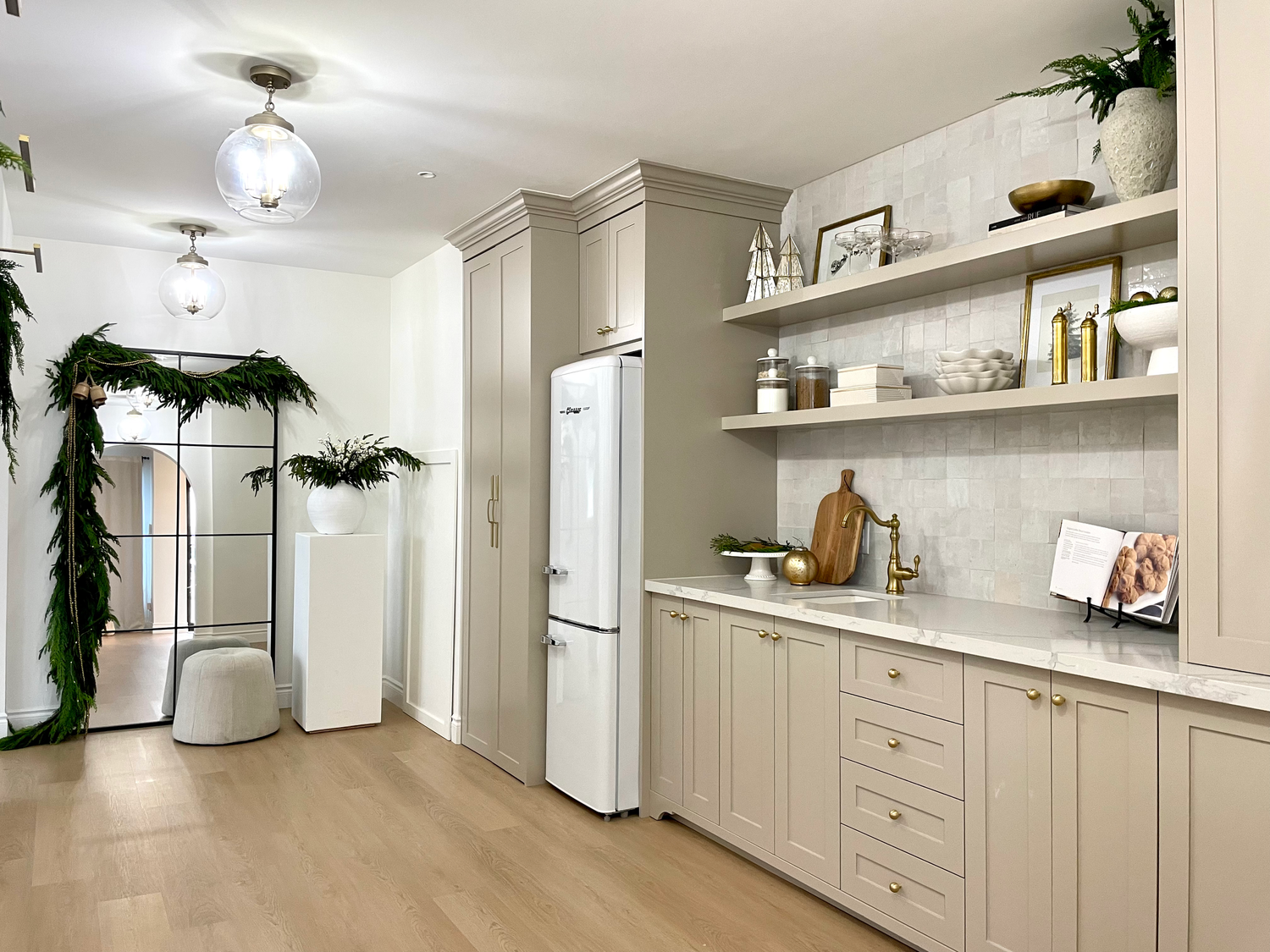 Modern kitchen interior with beige cabinets, white appliances, floating shelves and hardwood flooring.