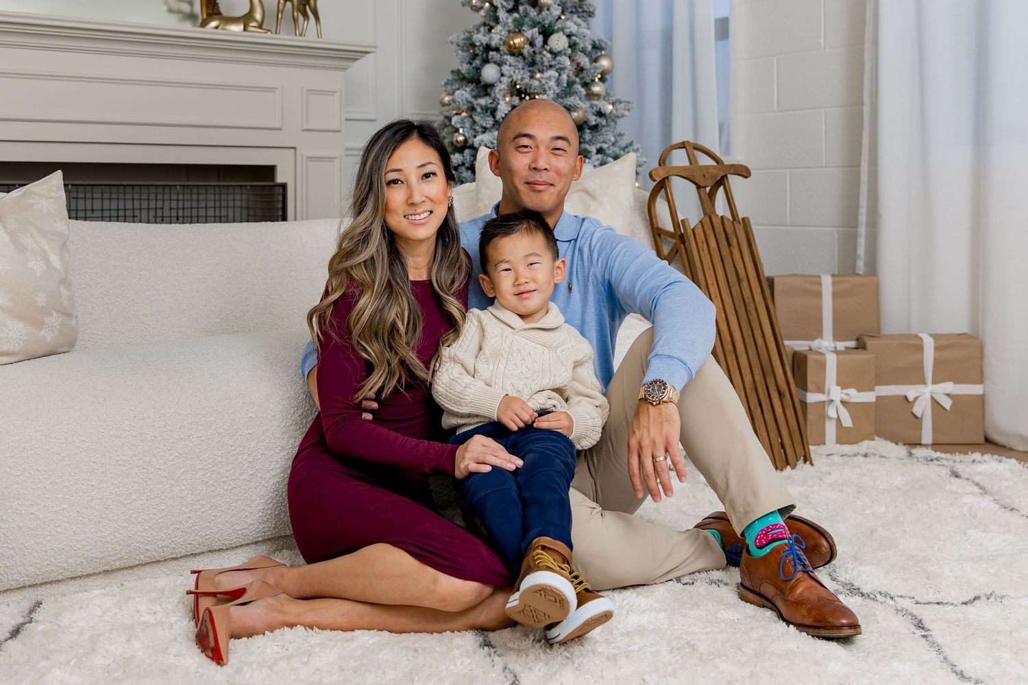 A family sits together on the floor in front of a Christmas tree in a cozy living room decorated for the holidays.