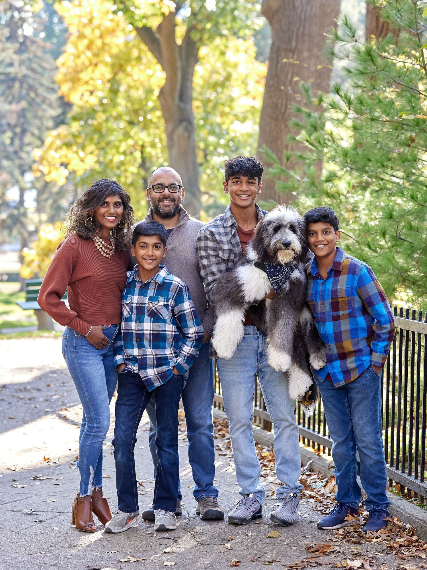 A family group with their large fluffy sheepdog poses together on an autumn path with yellow foliage in the background in High Park.
